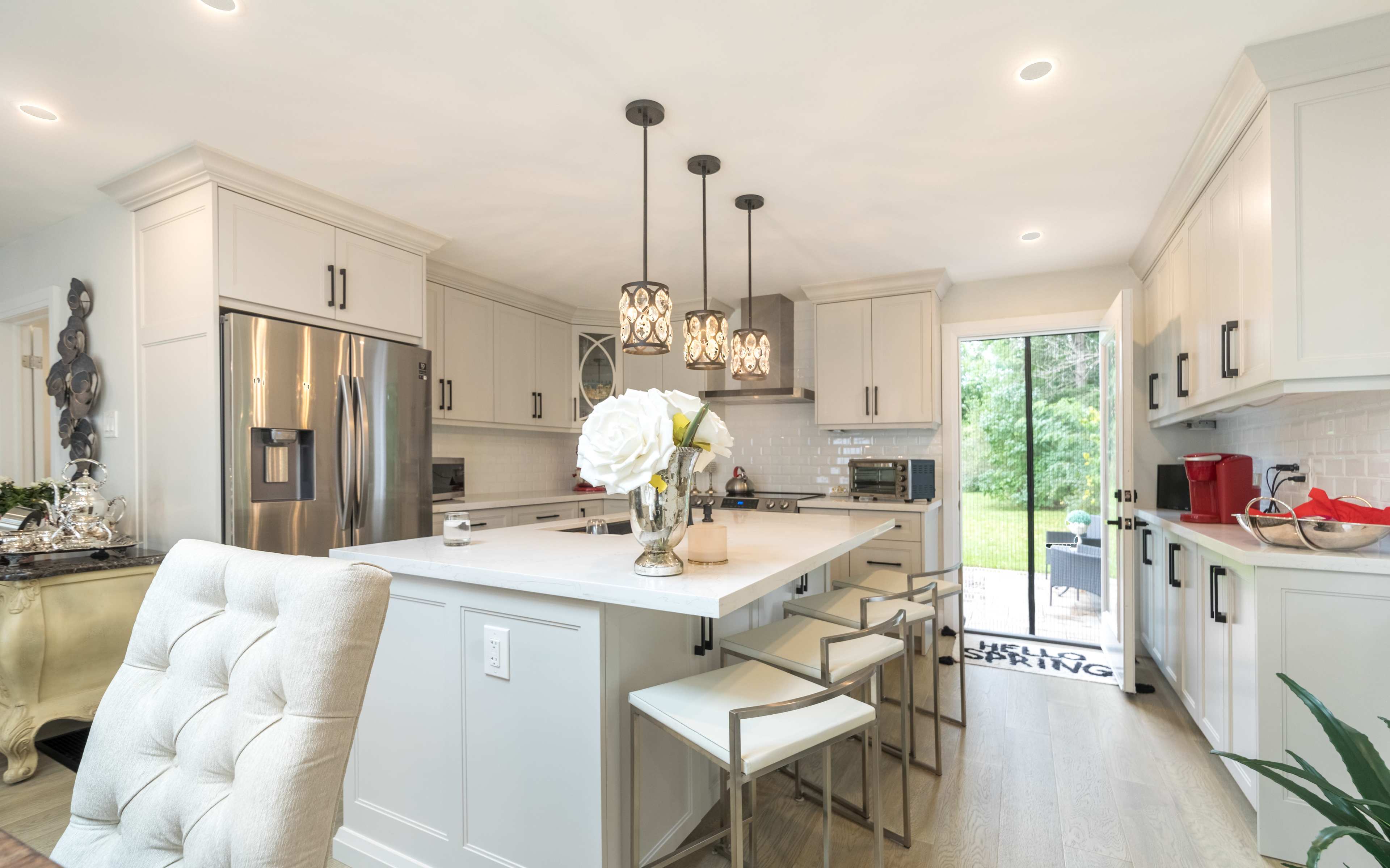 A modern kitchen featuring light cabinetry, a central island with seating, and large windows leading to an outdoor patio.