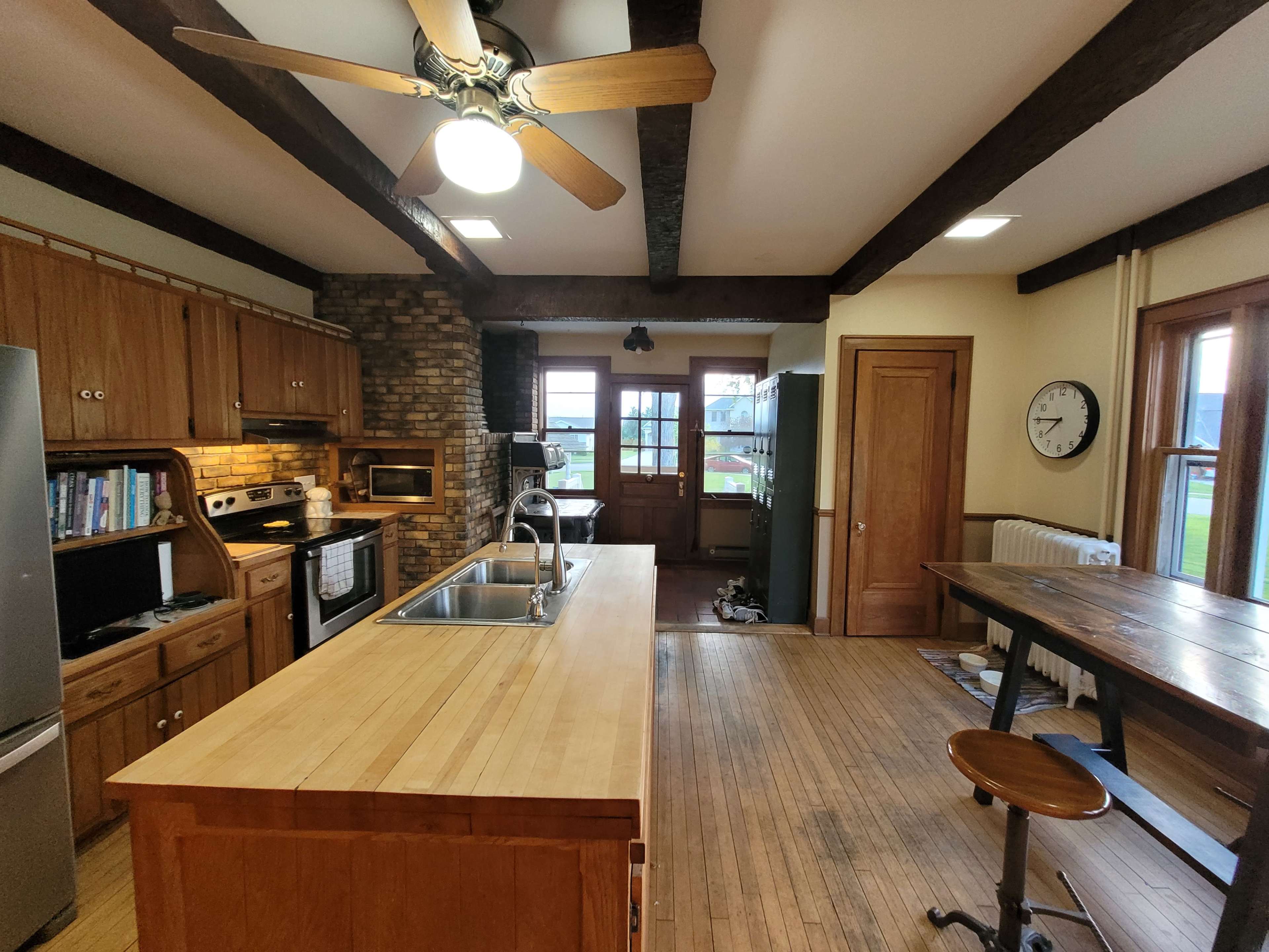 A spacious kitchen with wooden cabinets, a central island with a sink, and a combination of modern appliances against a backdrop of exposed wooden beams and a stone wall.