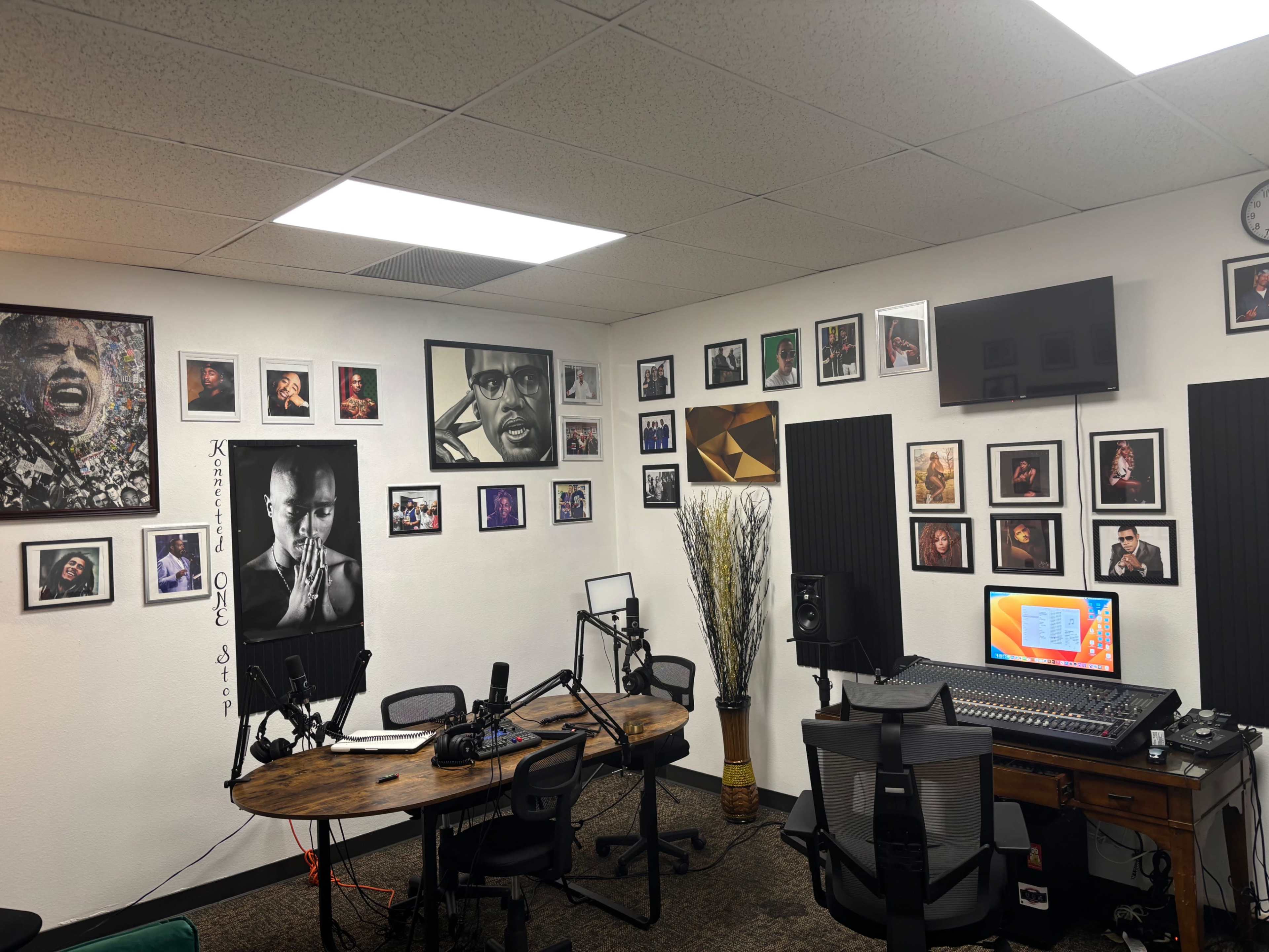 The image shows a recording studio with a large desk, audio equipment, several photographs of musicians on the walls, and a computer setup.