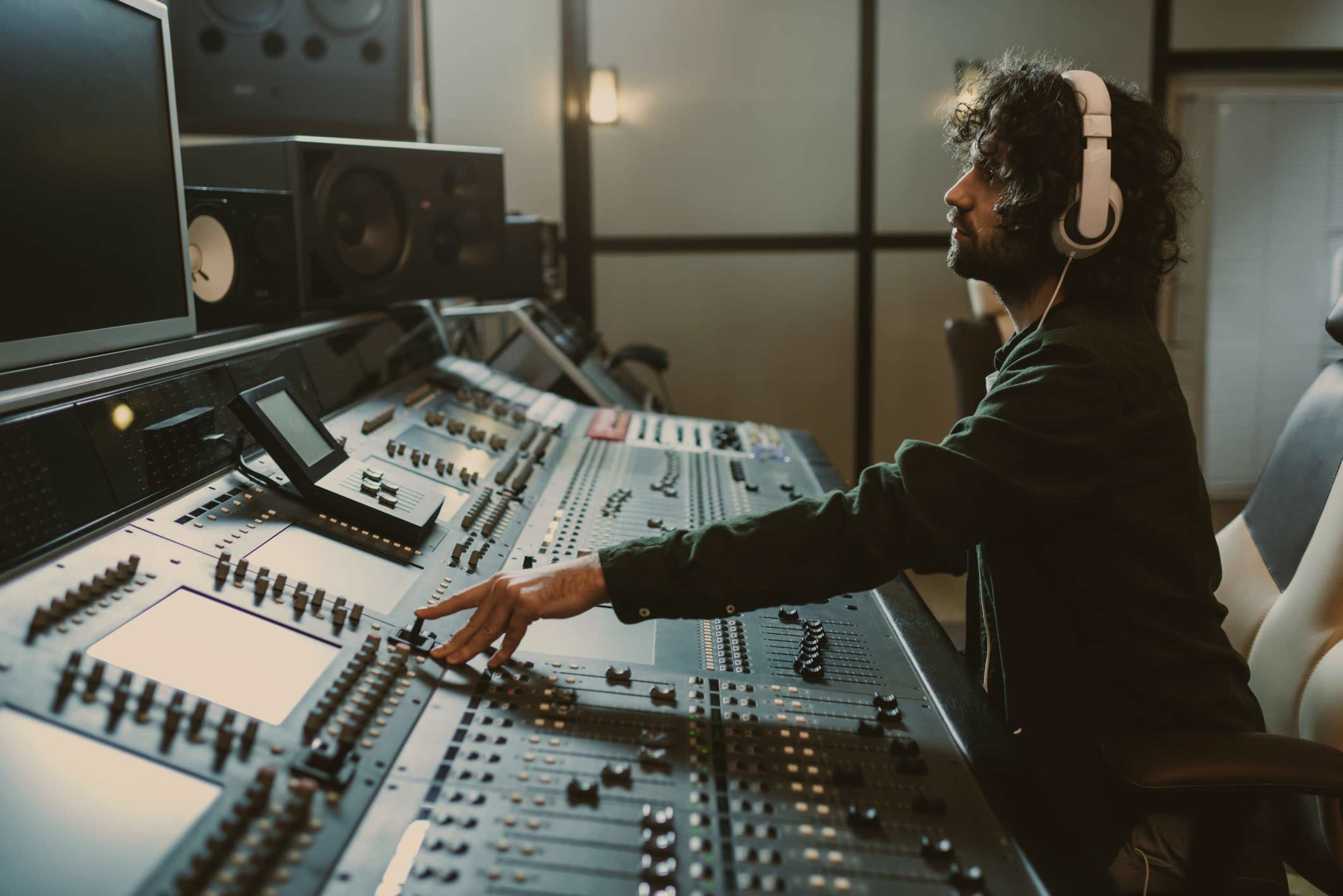 A person wearing headphones operates a sound mixing console in a recording studio.