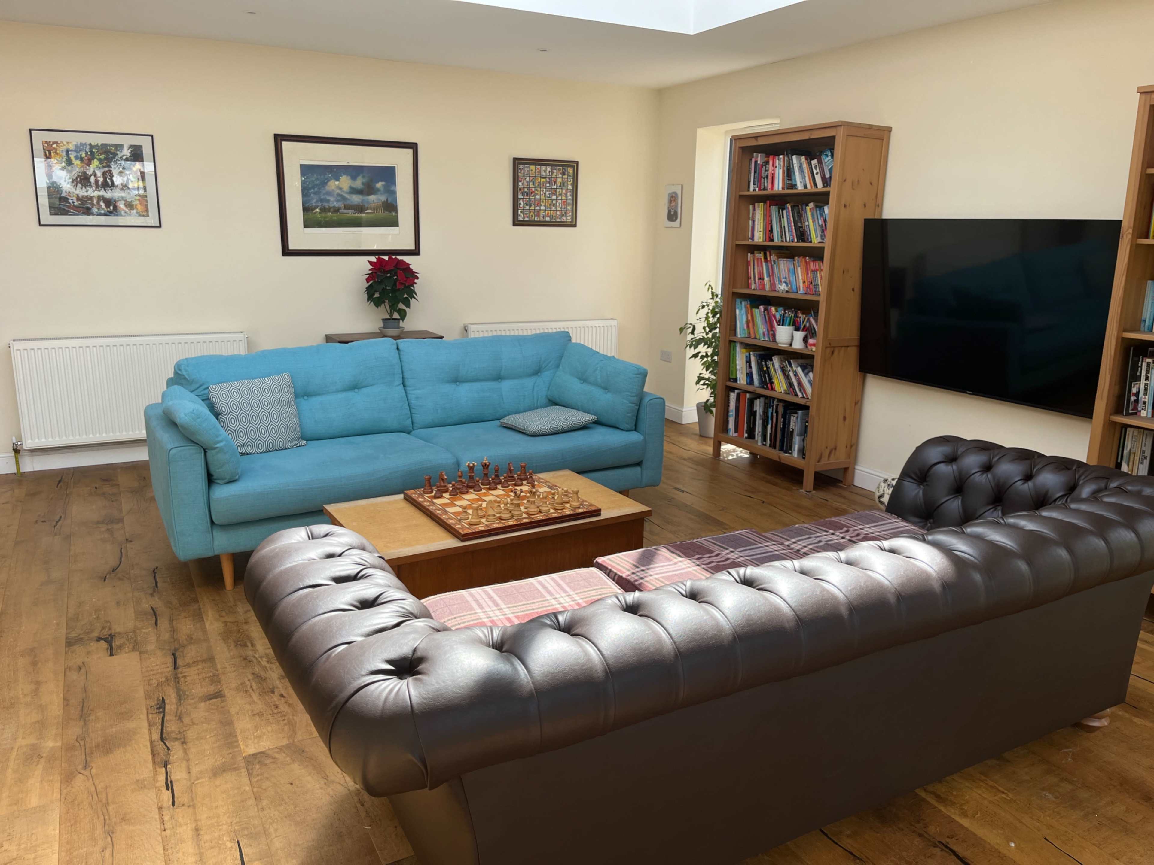 The room features a turquoise couch and a dark brown leather sofa arranged around a wooden chess table, with bookshelves and framed artwork on the walls.