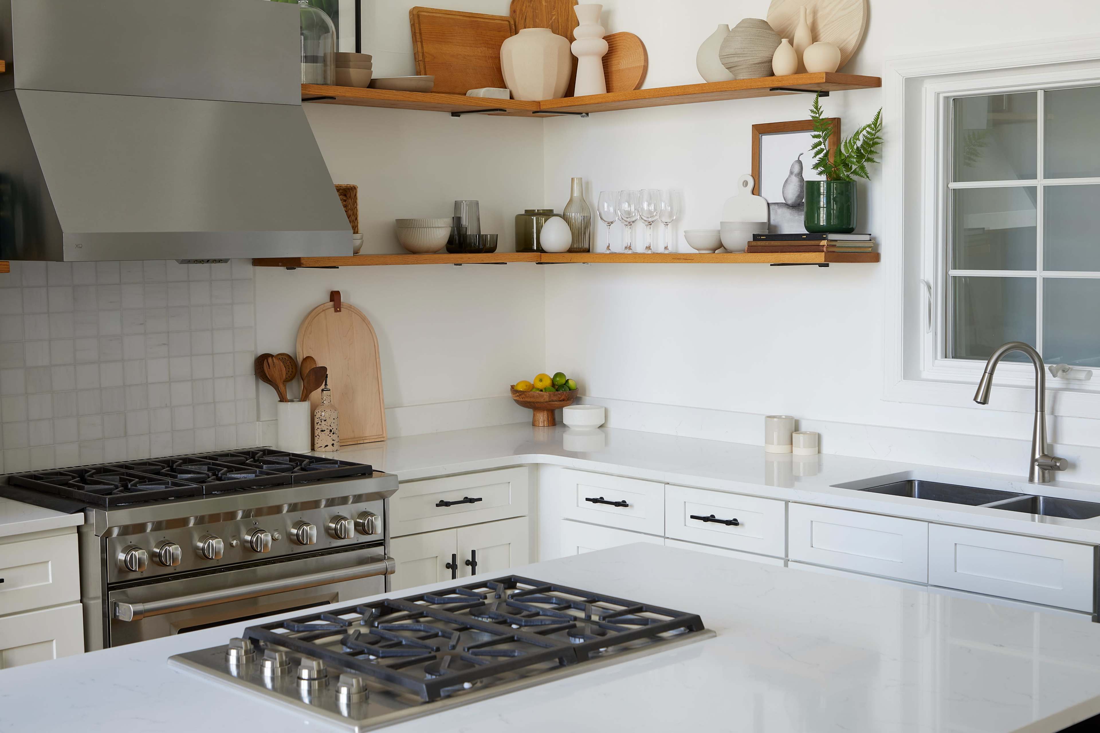 A modern kitchen with a gas stove, open shelving displaying decorative items, and a central island featuring a cooktop and a sink.