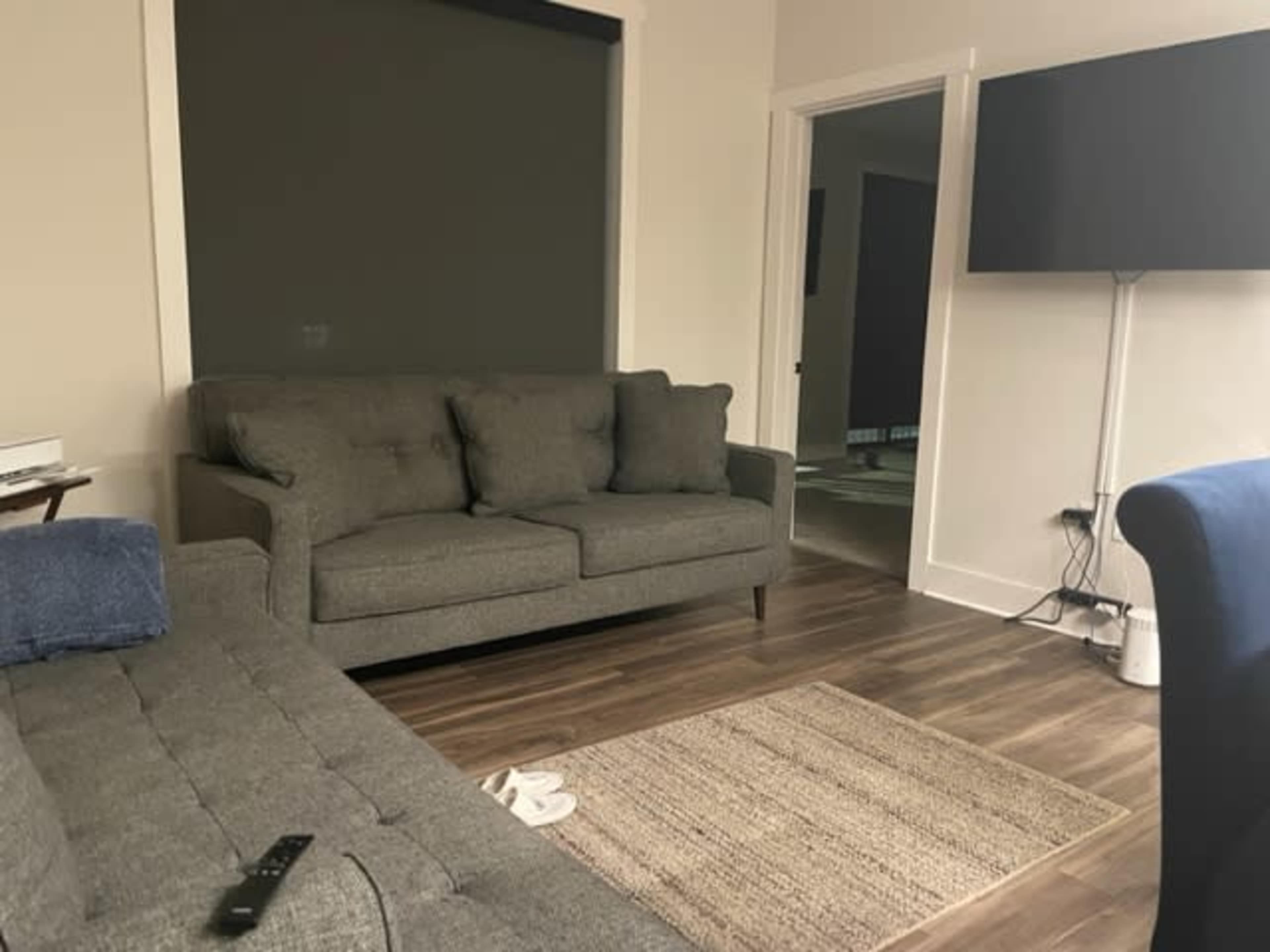 A living room with two gray sofas, a television mounted on the wall, and a light-colored rug on a wooden floor.