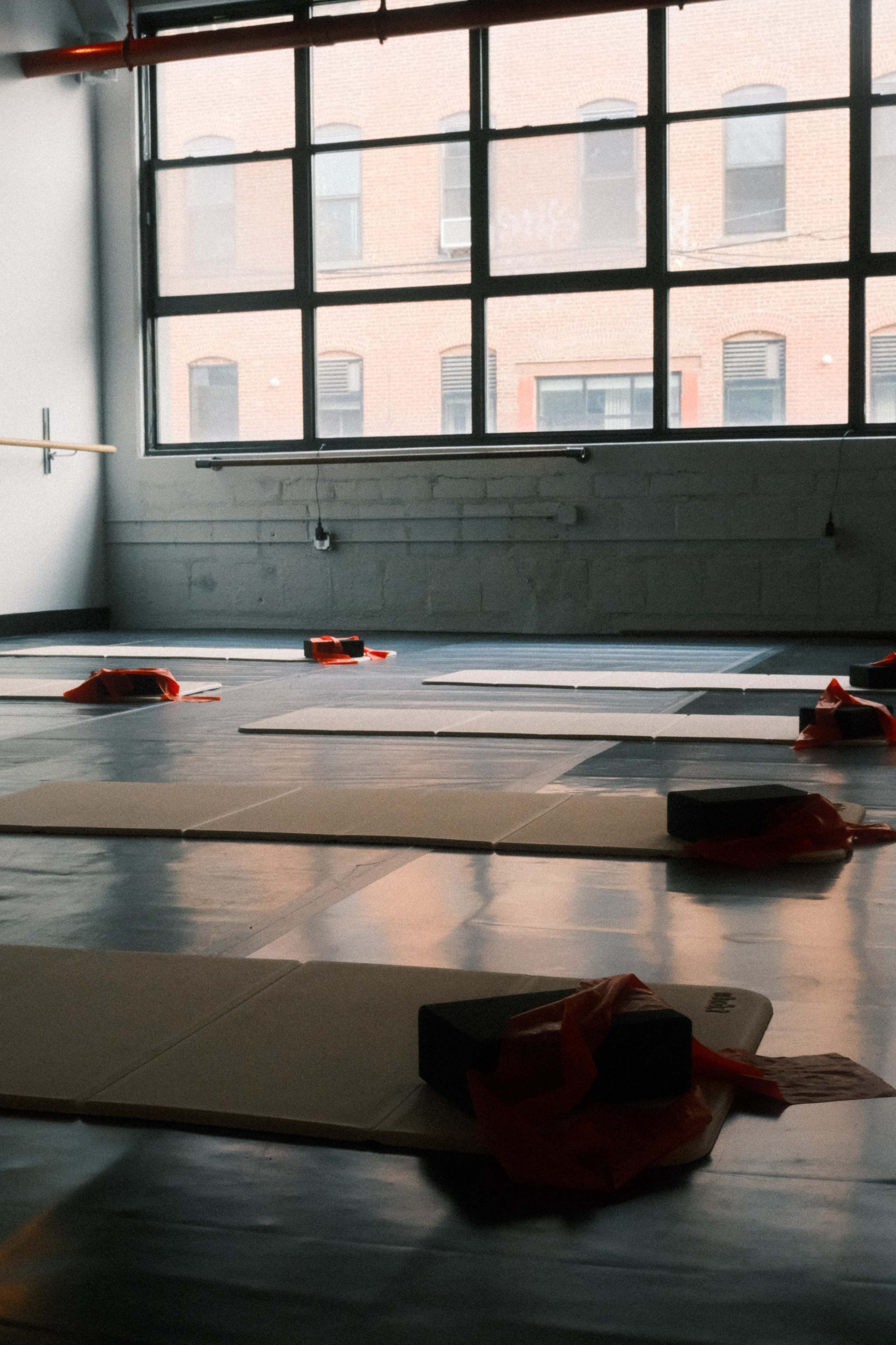 The image shows a yoga studio with several mats arranged on the floor and yoga blocks near the windows.