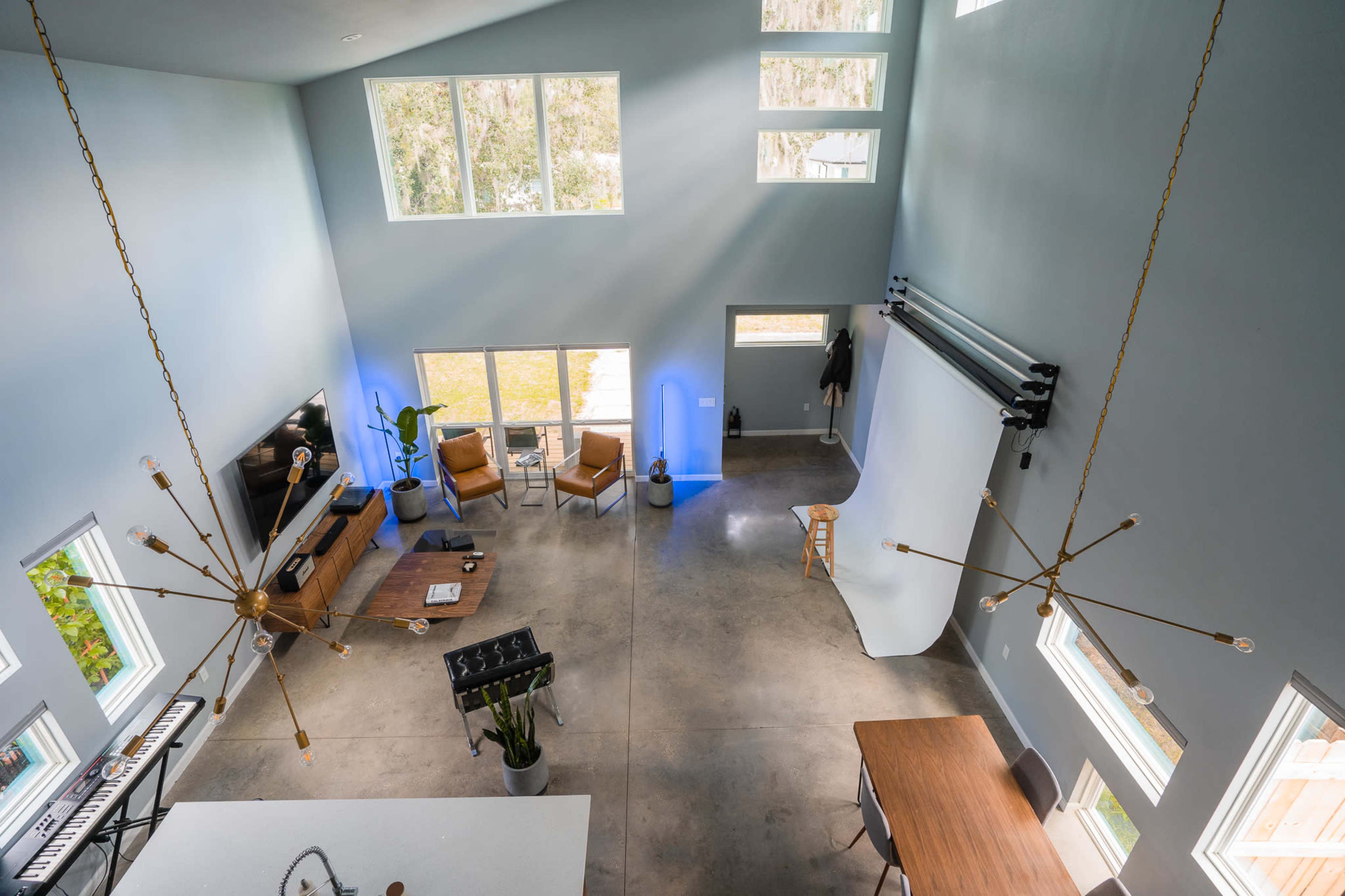 A spacious room with high ceilings, large windows, and a mix of modern furniture, including chairs, a dining table, and studio equipment.