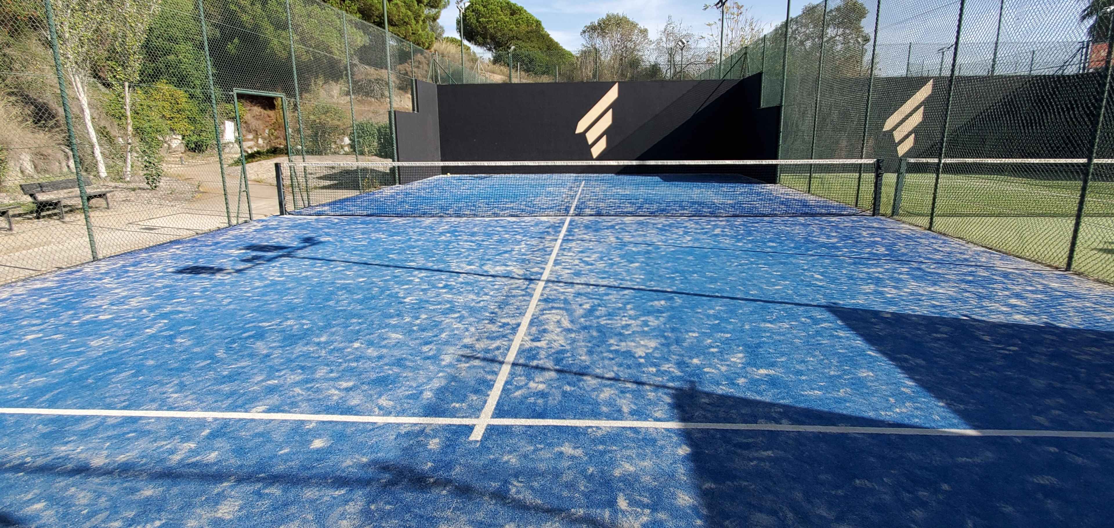 A blue paddle tennis court with a faded surface and a black wall at the back.