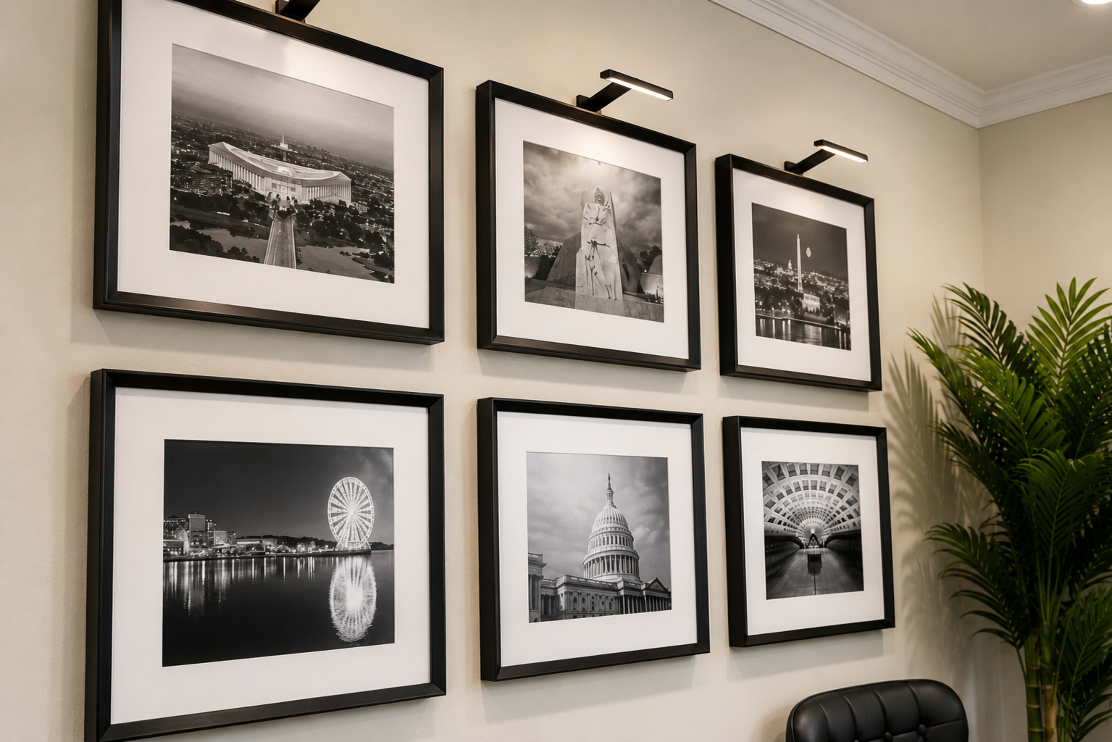 The image displays a wall with six black and white framed photographs, each featuring different landmarks and urban scenes, illuminated by wall-mounted lights.