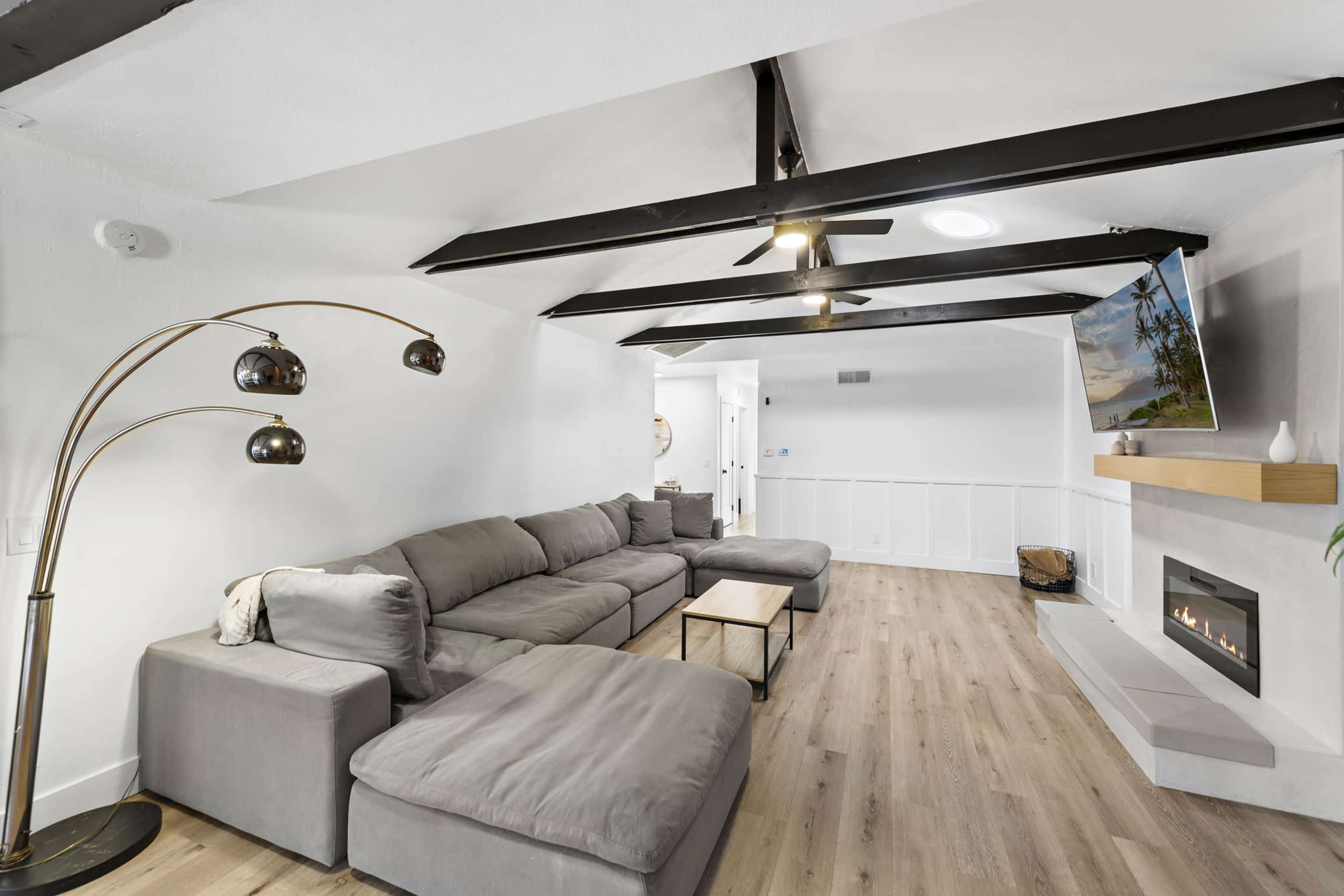 The image shows a modern living room with a sectional sofa, a coffee table, a wall-mounted TV, and a minimalist fireplace.