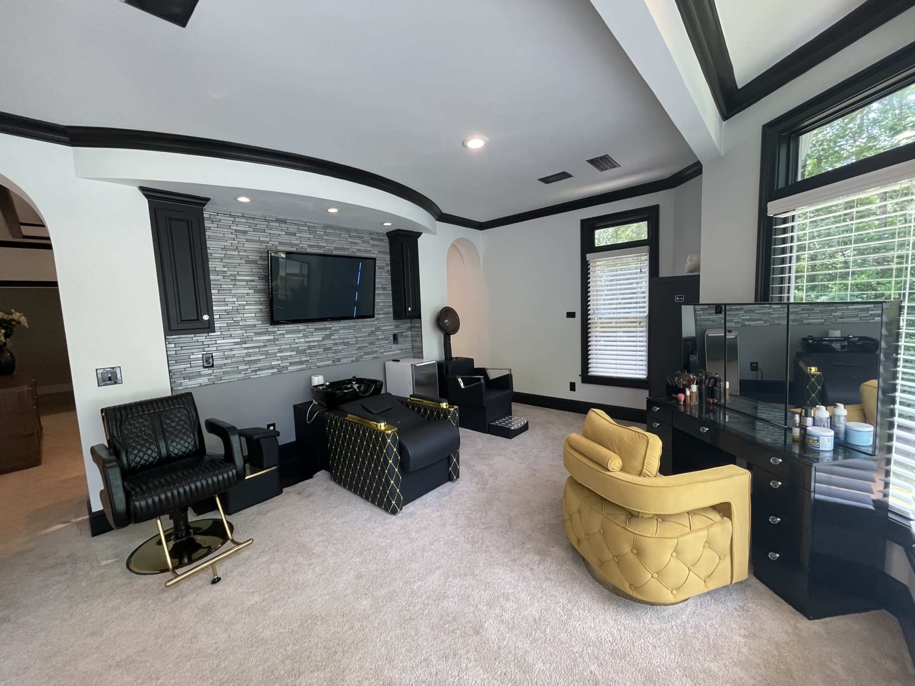 The image shows a stylish room featuring black and yellow furniture, a wall-mounted television, and large windows with natural light.