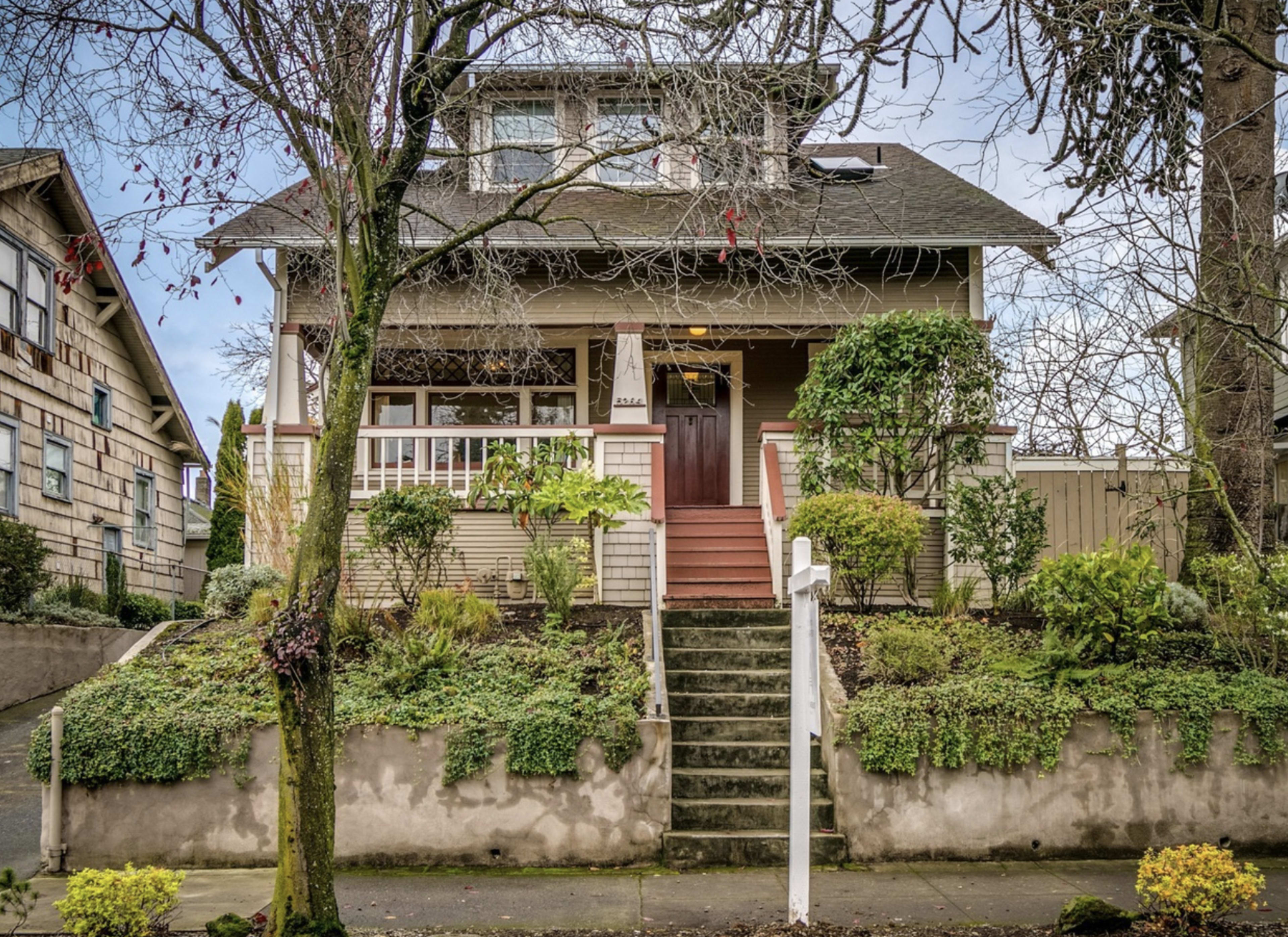 A two-story house with a front porch and landscaped garden is shown, featuring stairs leading up to the entrance.