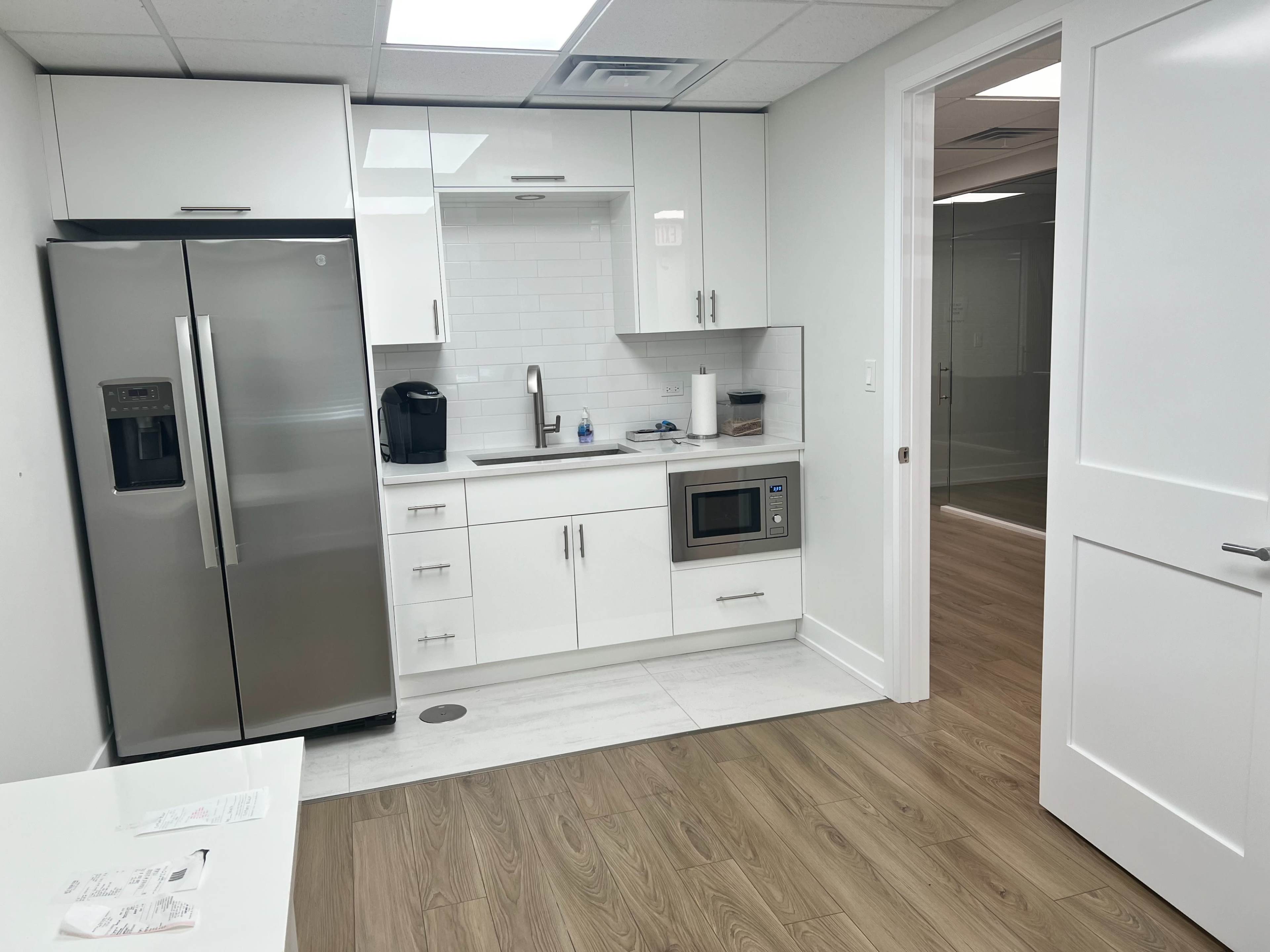 A modern kitchen equipped with stainless steel appliances, a microwave, and white cabinetry, adjacent to a door leading to another room.