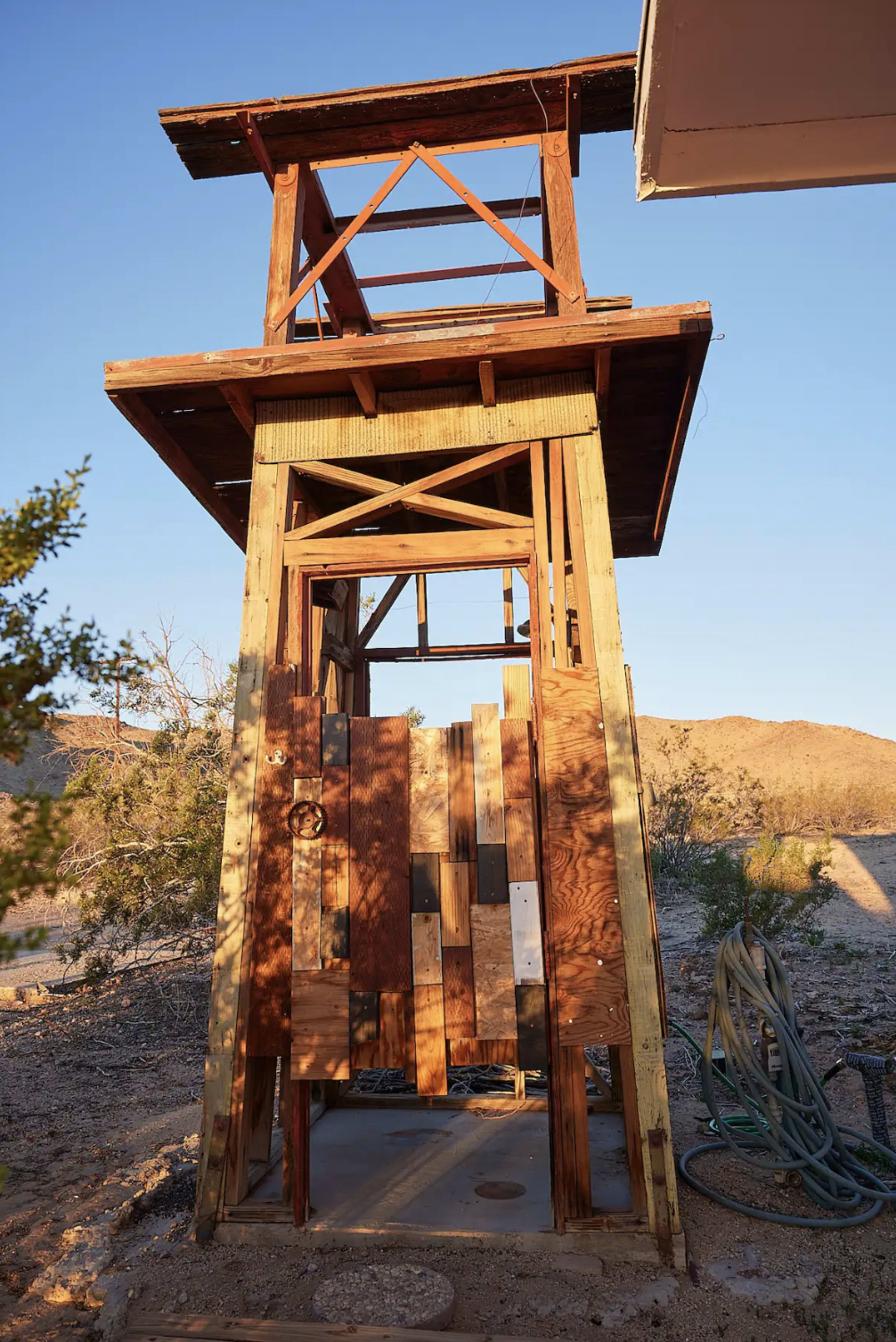 The image shows a wooden watchtower structure in a desert landscape, with a partially open door and construction materials visible.