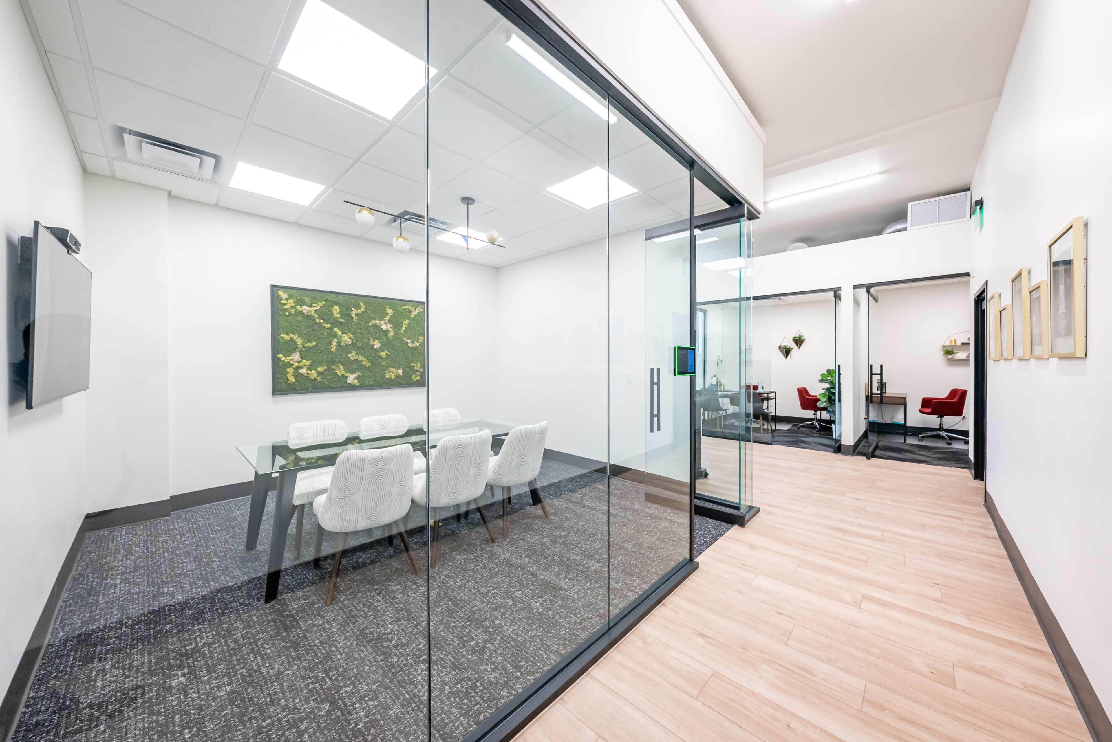 A modern office space features a glass-encased conference room with a table and chairs, alongside an open area with additional workstations.