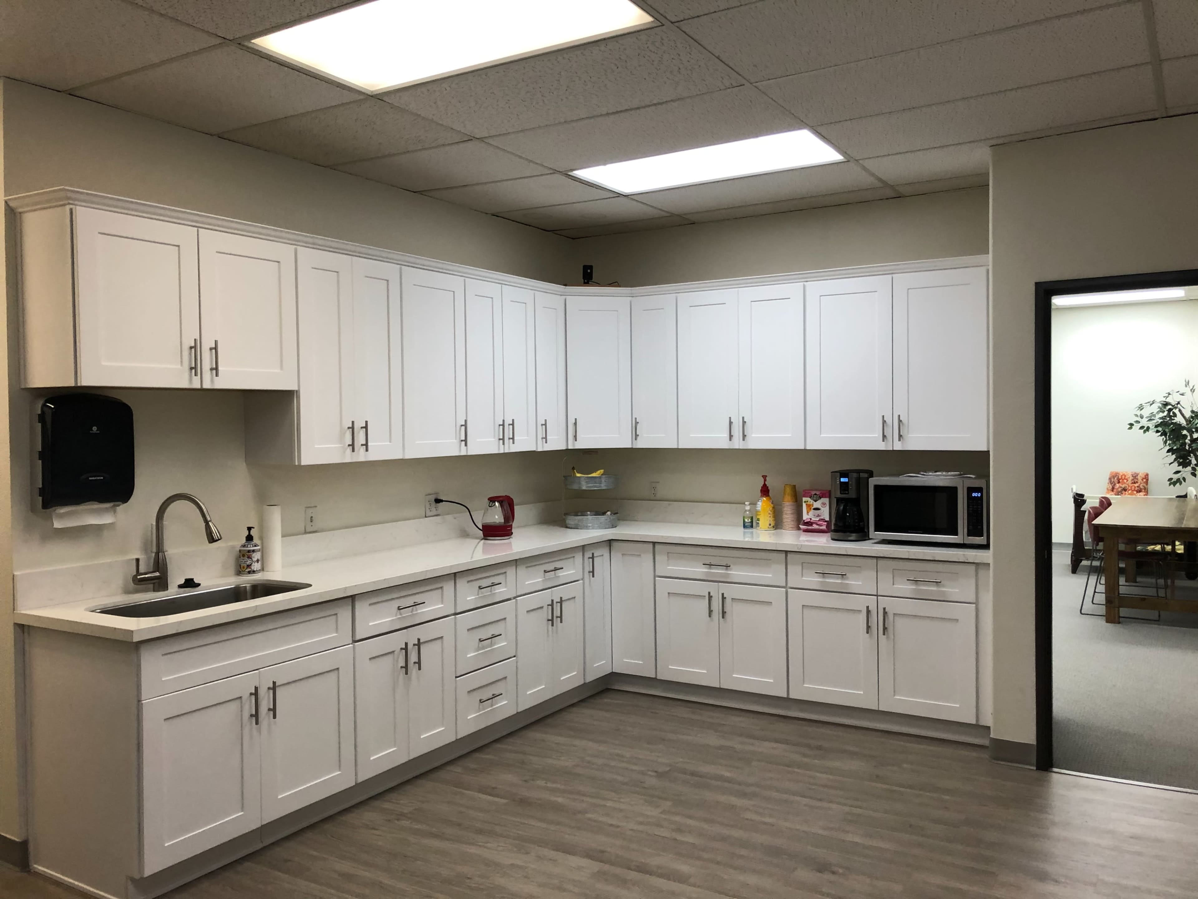 The image depicts a modern kitchen with white cabinetry, a sink, a countertop, and appliances including a microwave and a coffee maker.