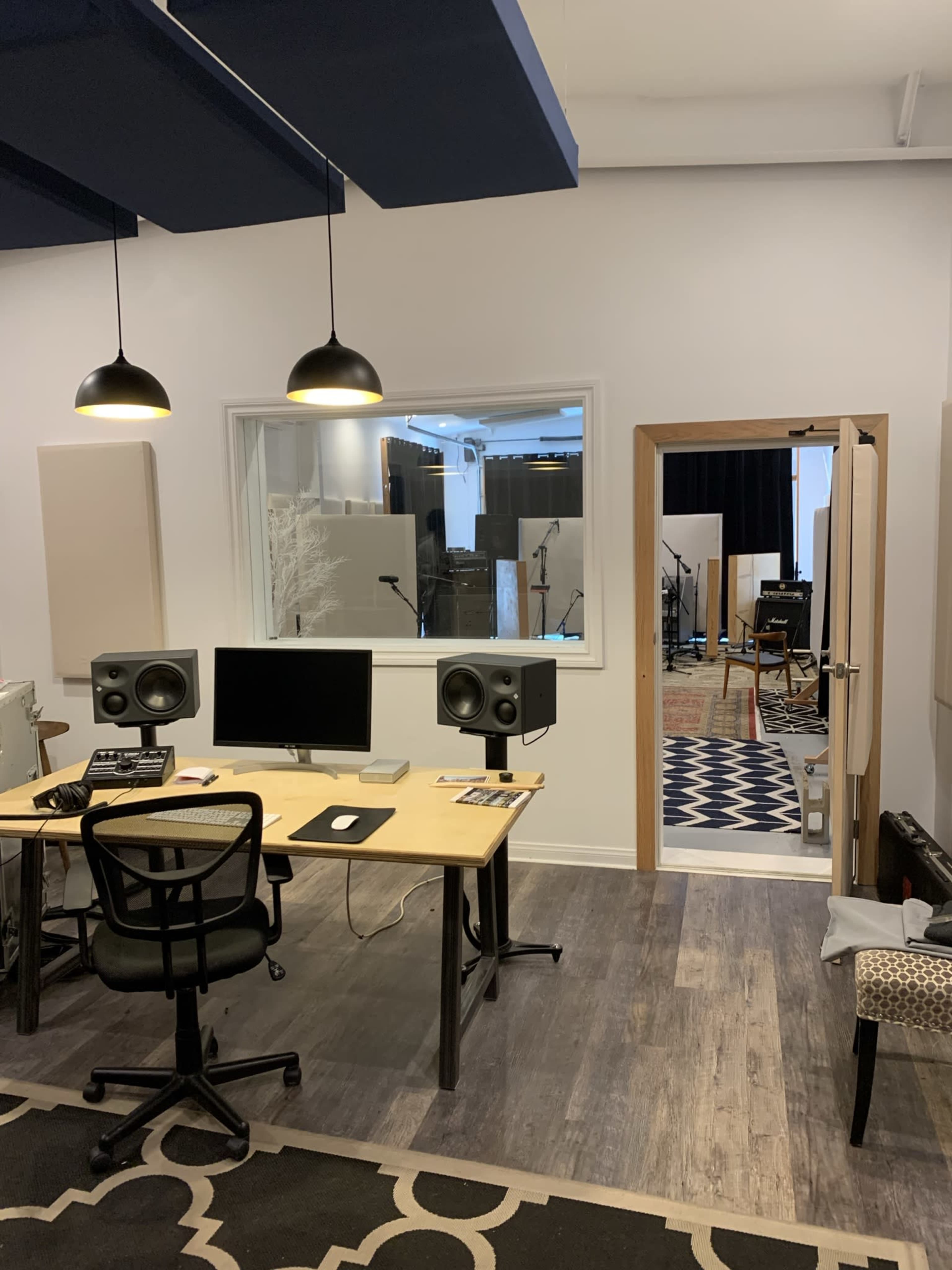 A music studio is shown with a desk featuring a computer and speakers, and a door leading to another room with musical instruments visible.