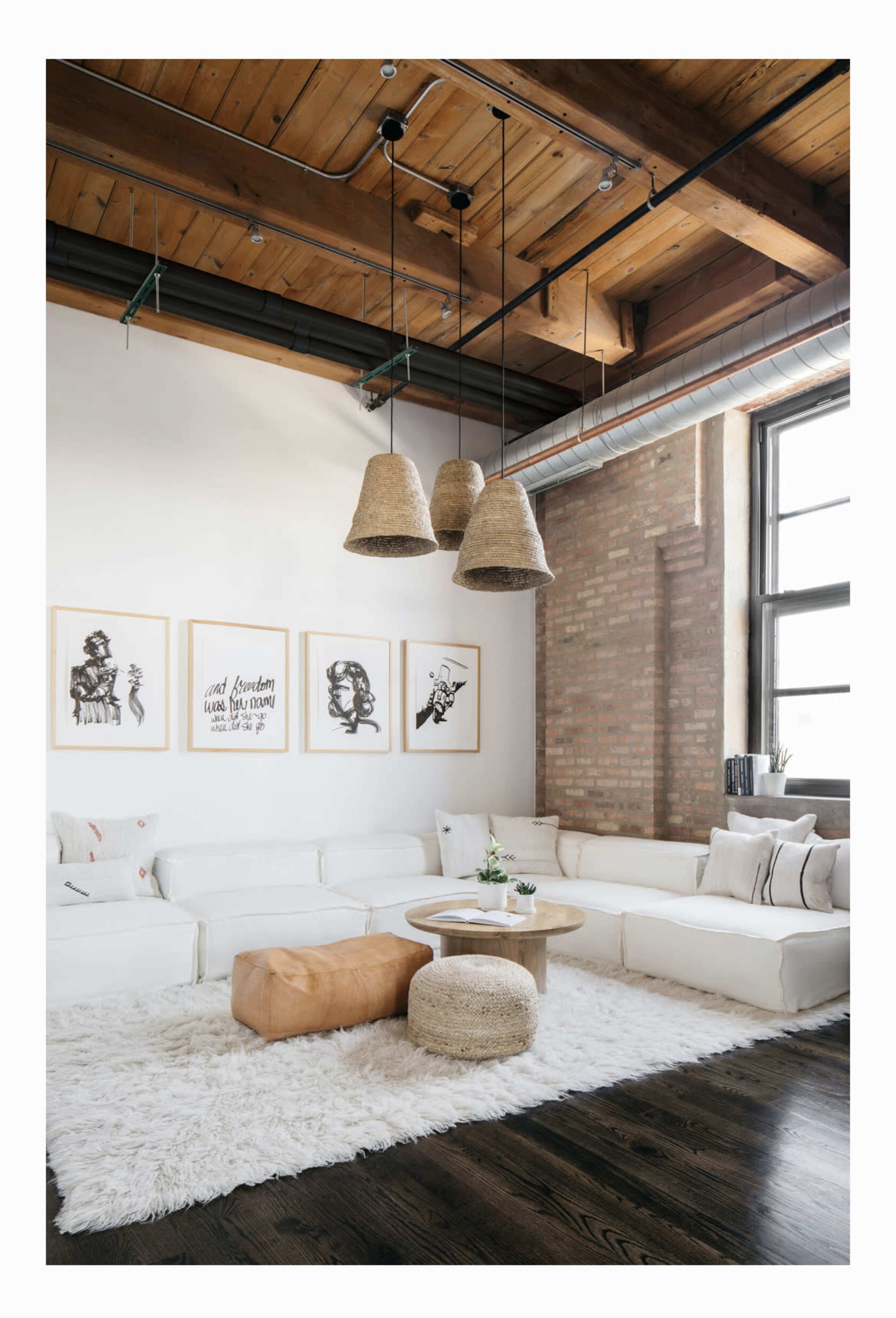 A modern living room features a white sectional sofa, a round coffee table, and three large pendant lights hanging from the ceiling, with artwork displayed on the walls and a plush rug on the floor.
