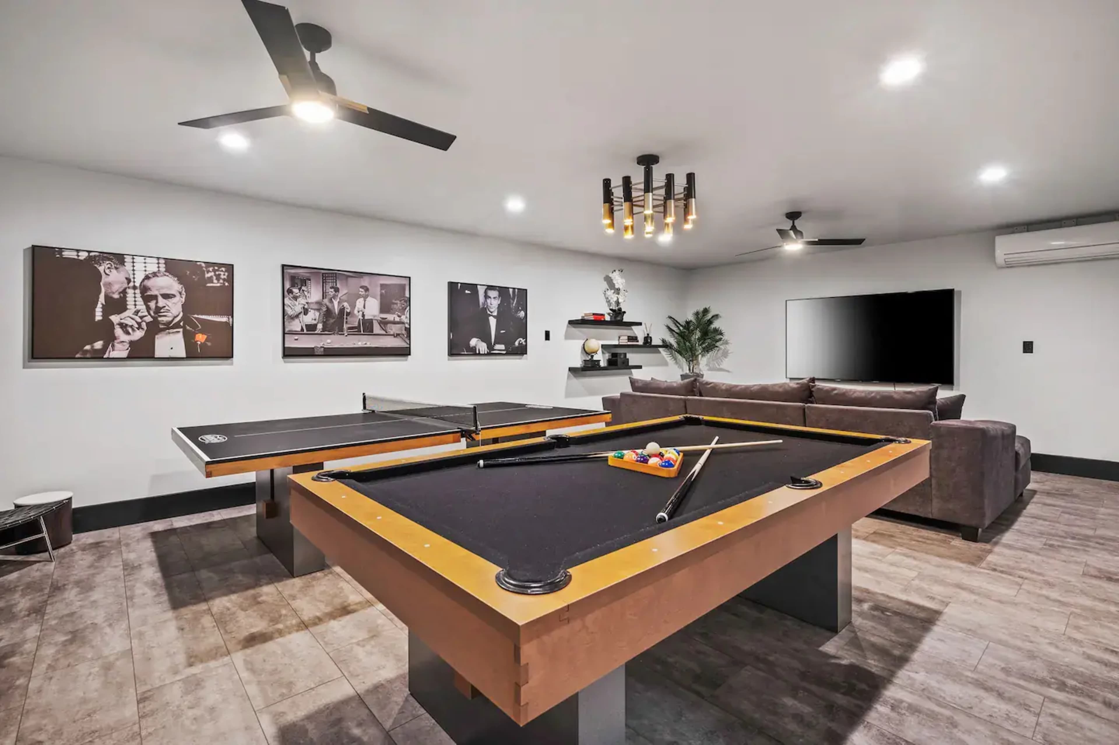 A game room with a pool table, a ping pong table, a sofa, and black-and-white wall art.
