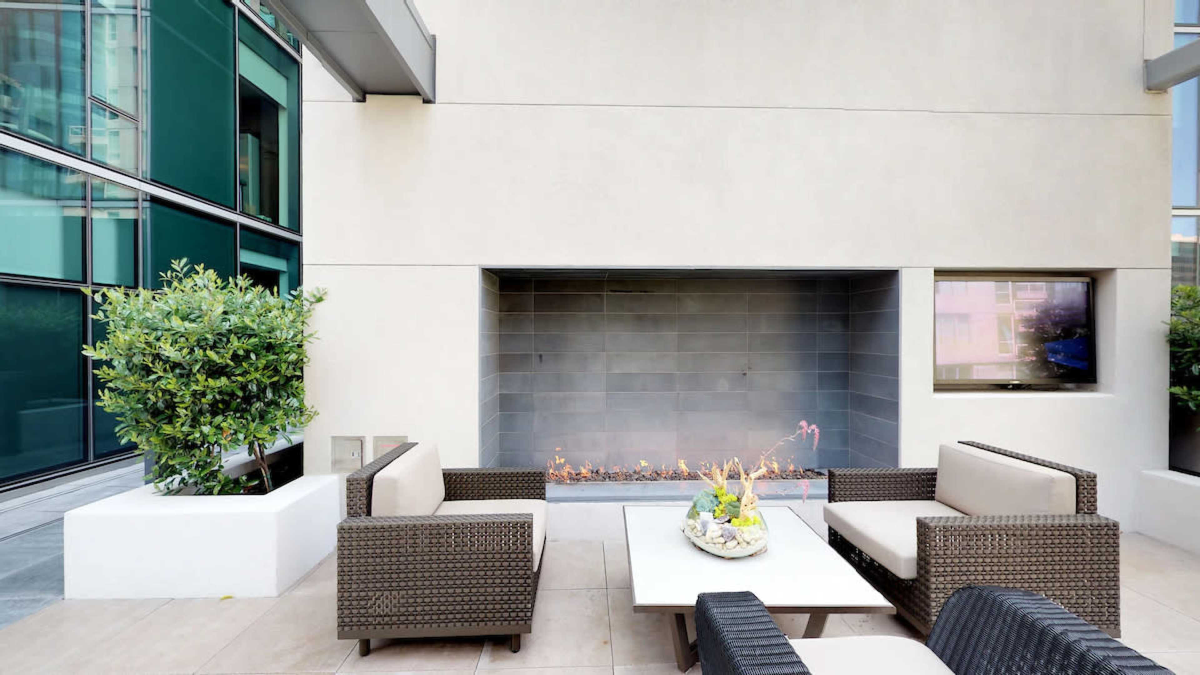 A modern outdoor seating area featuring a table and two sofas arranged around a gas fireplace.