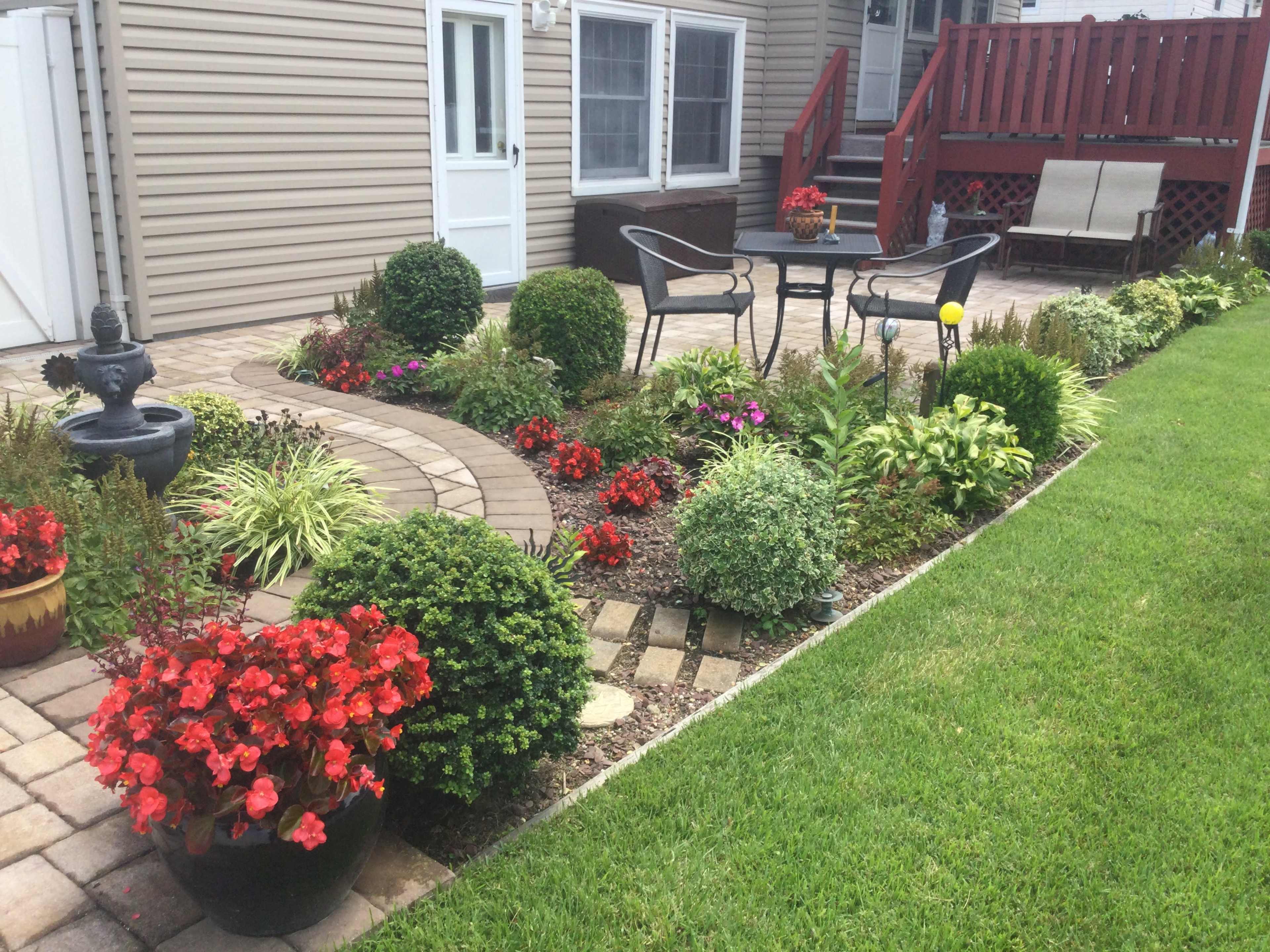 A well-designed garden features a winding stone path, neatly trimmed shrubs, colorful flower beds, and a seating area with a table and chairs.