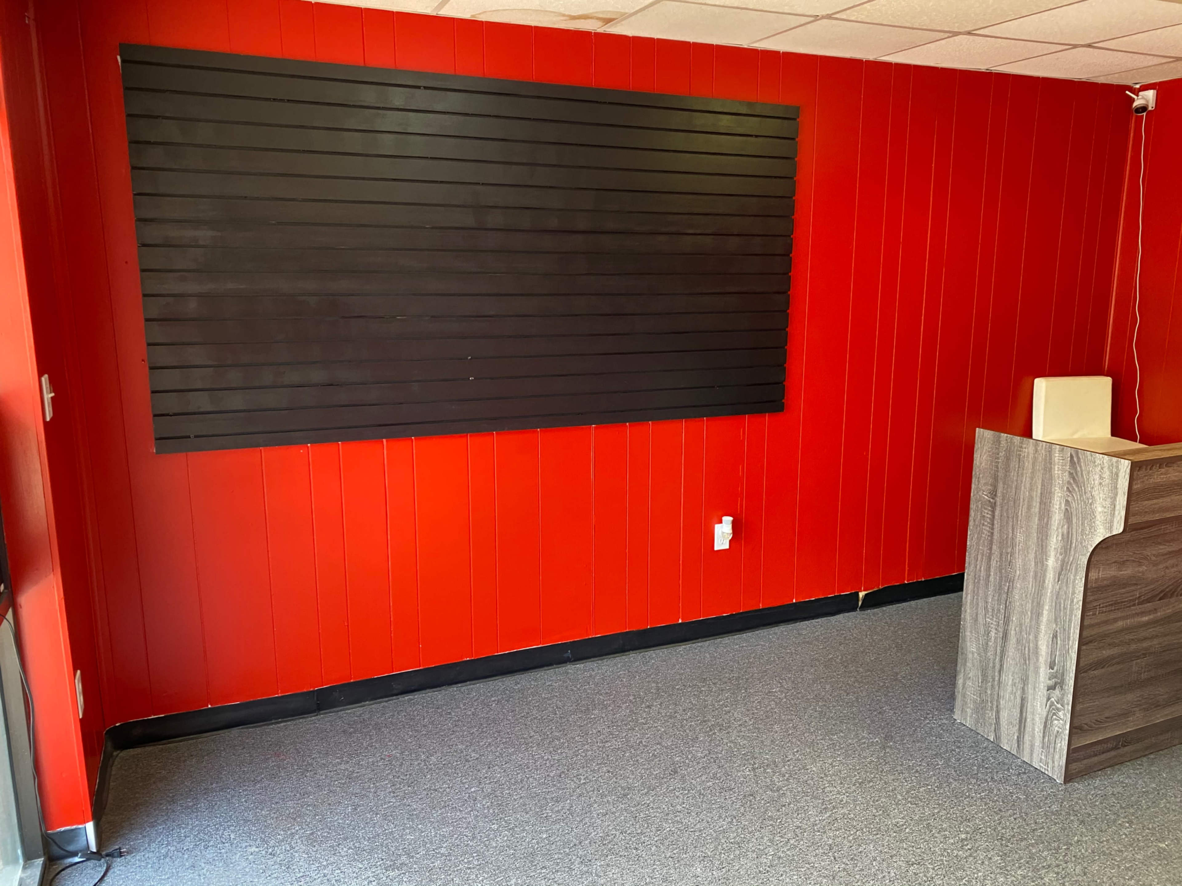 An empty room with red walls, a black slat wall, and a wooden reception counter in a corner.