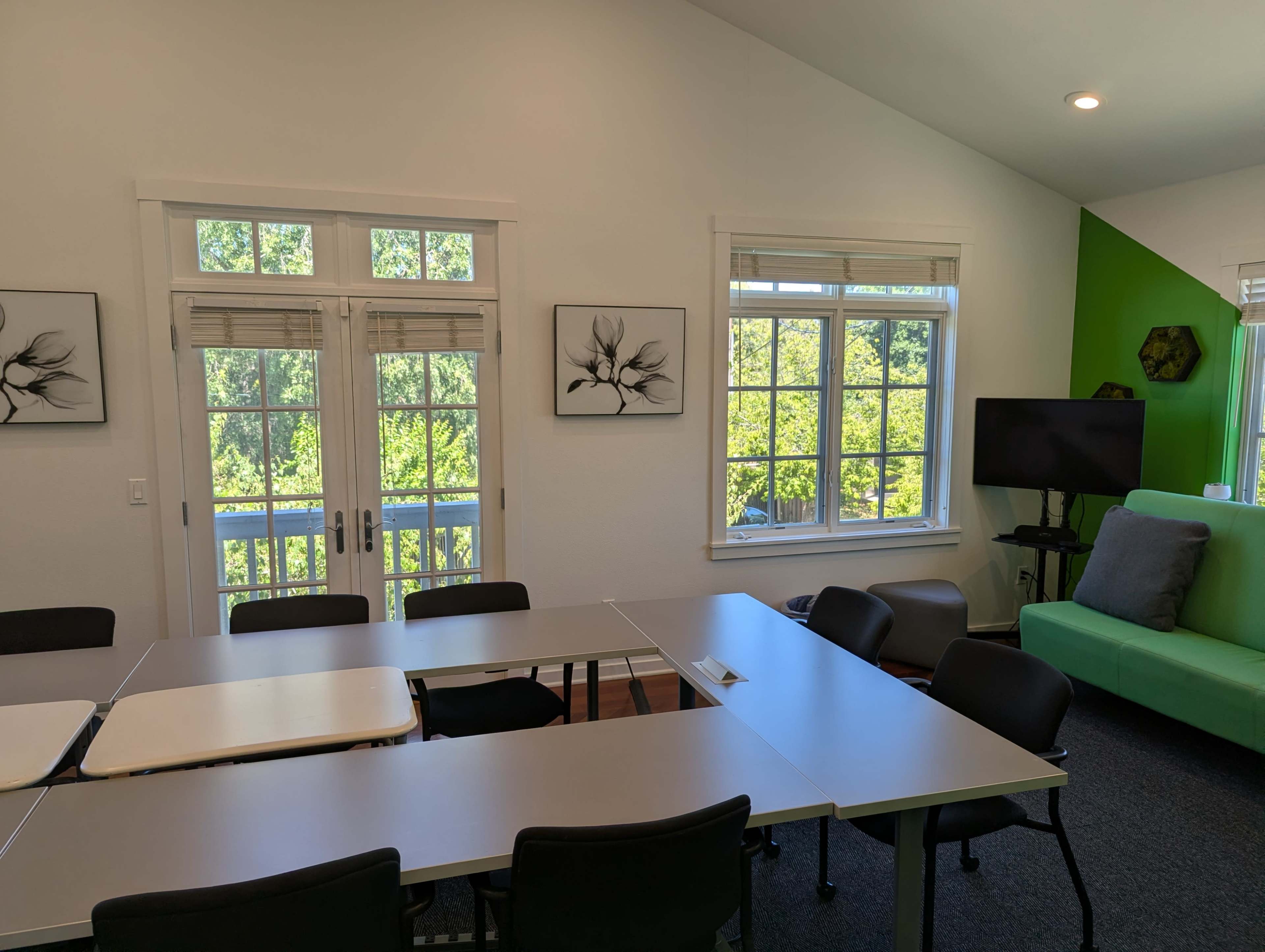 A spacious meeting room features a long table surrounded by black chairs, with large windows that offer a view of greenery outside.