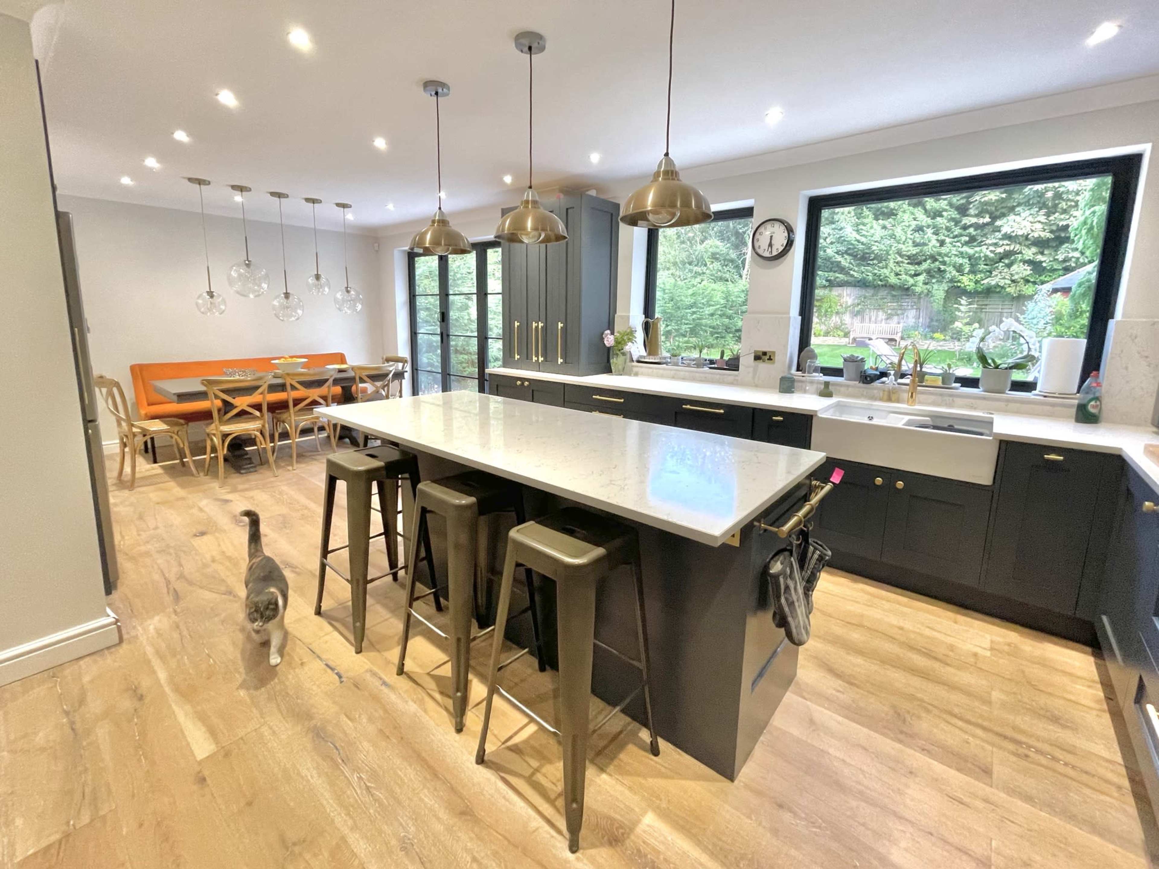 A modern kitchen features a central island with bar stools, pendant lighting, and a dining area in the background.