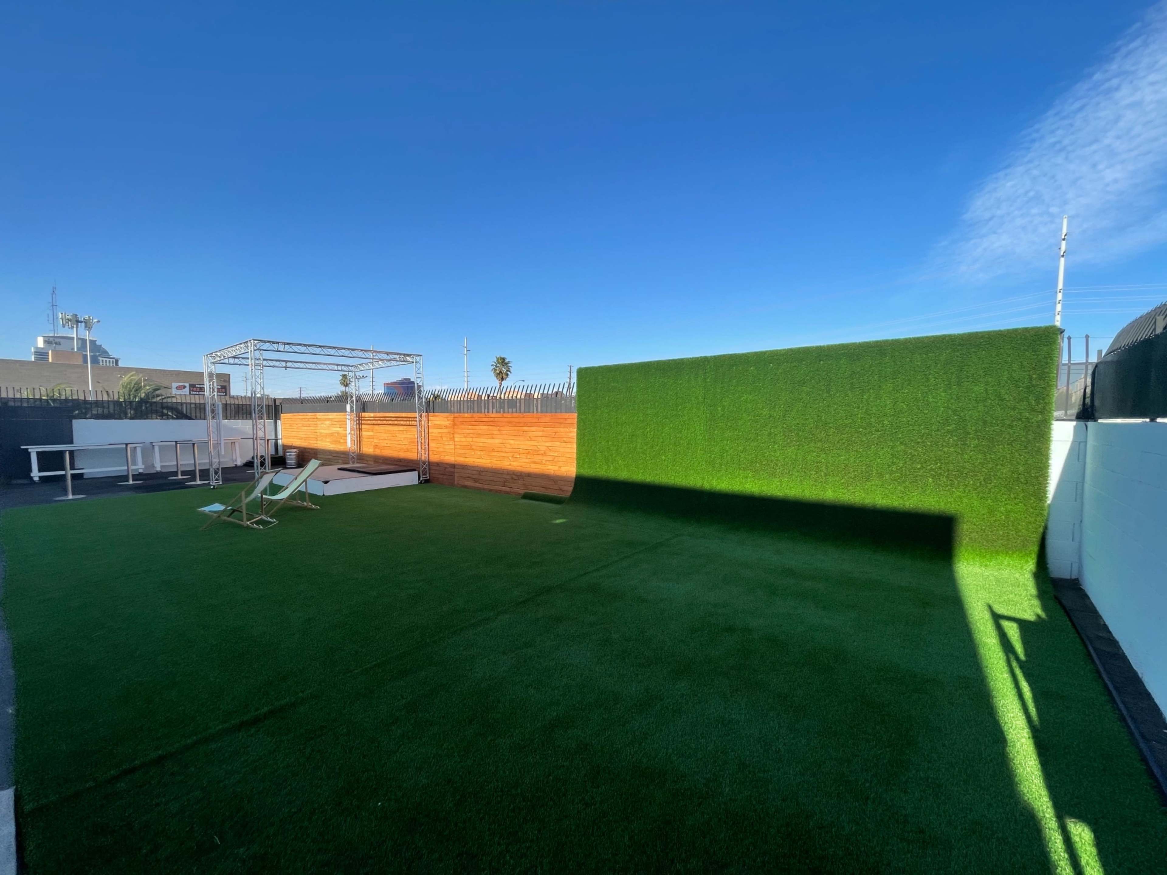 A spacious outdoor area featuring artificial grass, a wooden fence, and a metal frame structure.