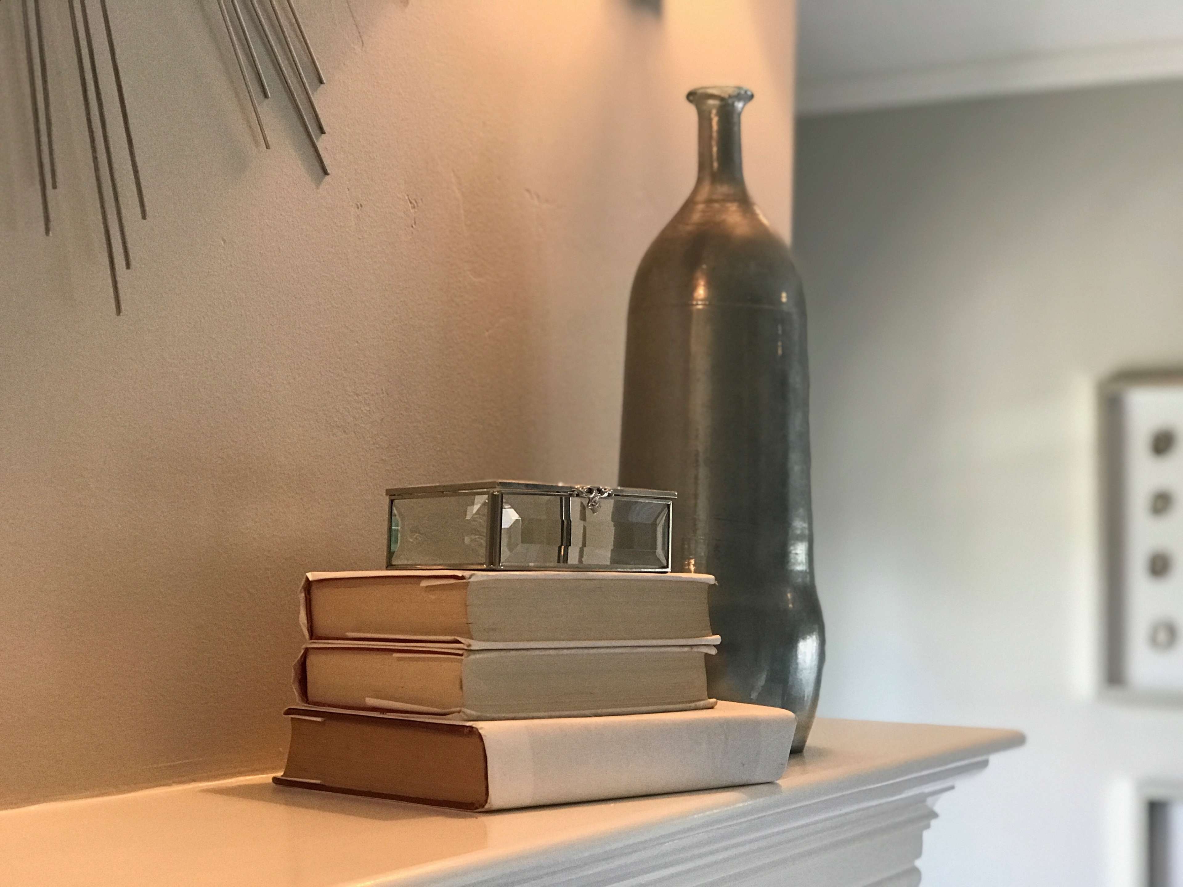 A stack of three books sits on a shelf next to a glass box and a large glass bottle.