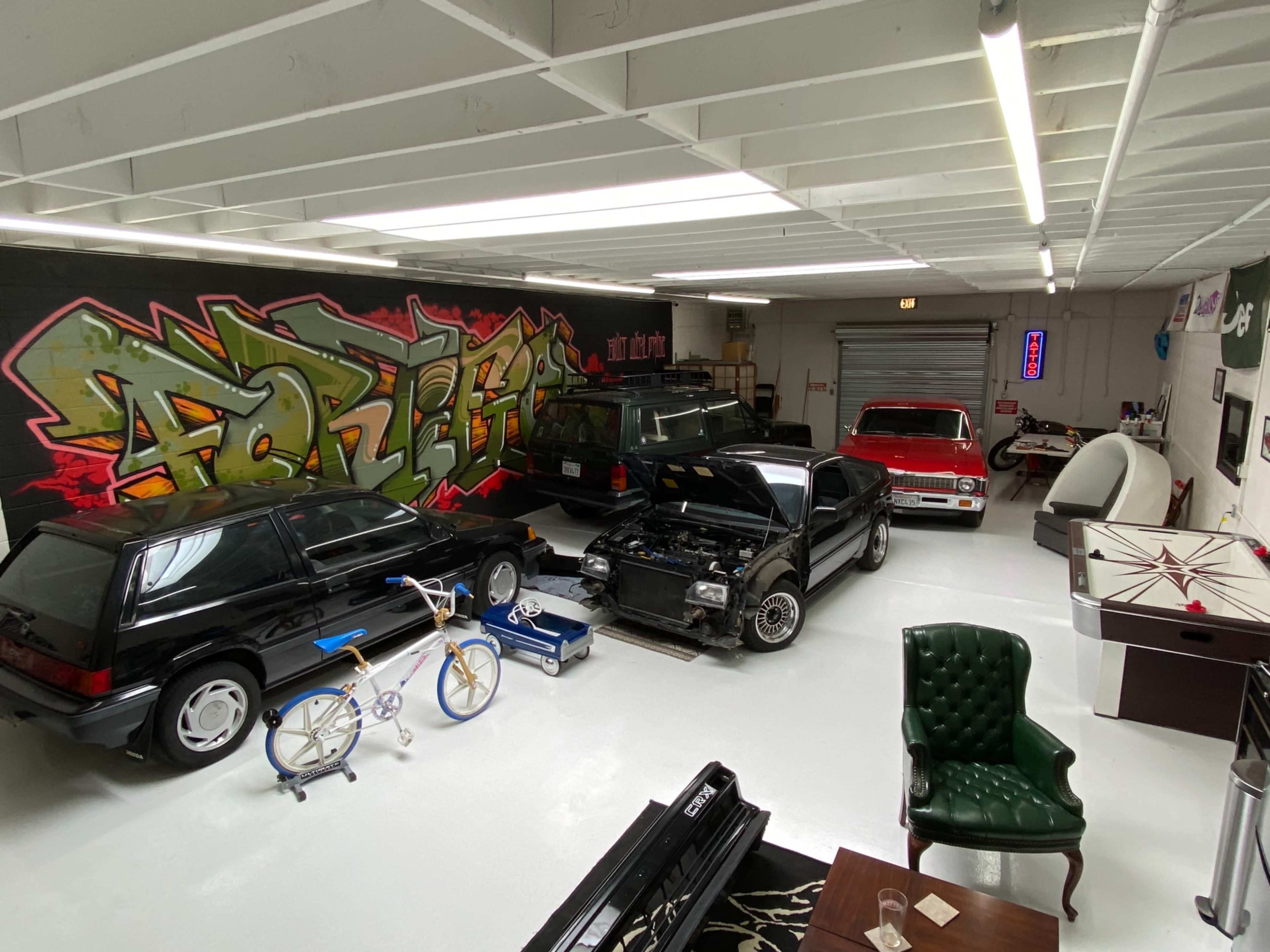 The garage features several parked cars, a motorcycle, bicycles, and a large wall adorned with colorful graffiti.