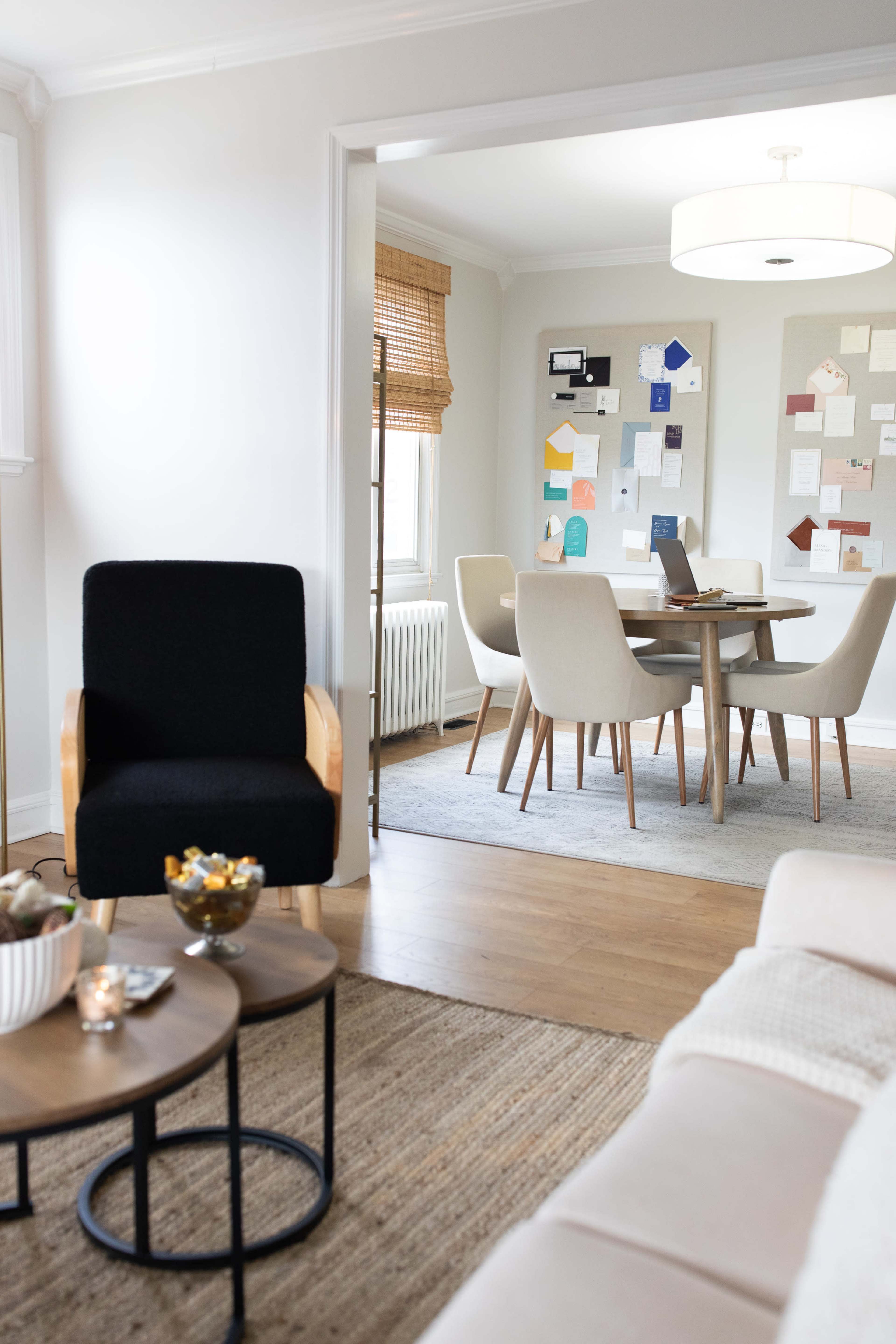 A cozy living space features a black armchair and a round coffee table, while a dining area with beige chairs and a light-colored table is visible through an open doorway.