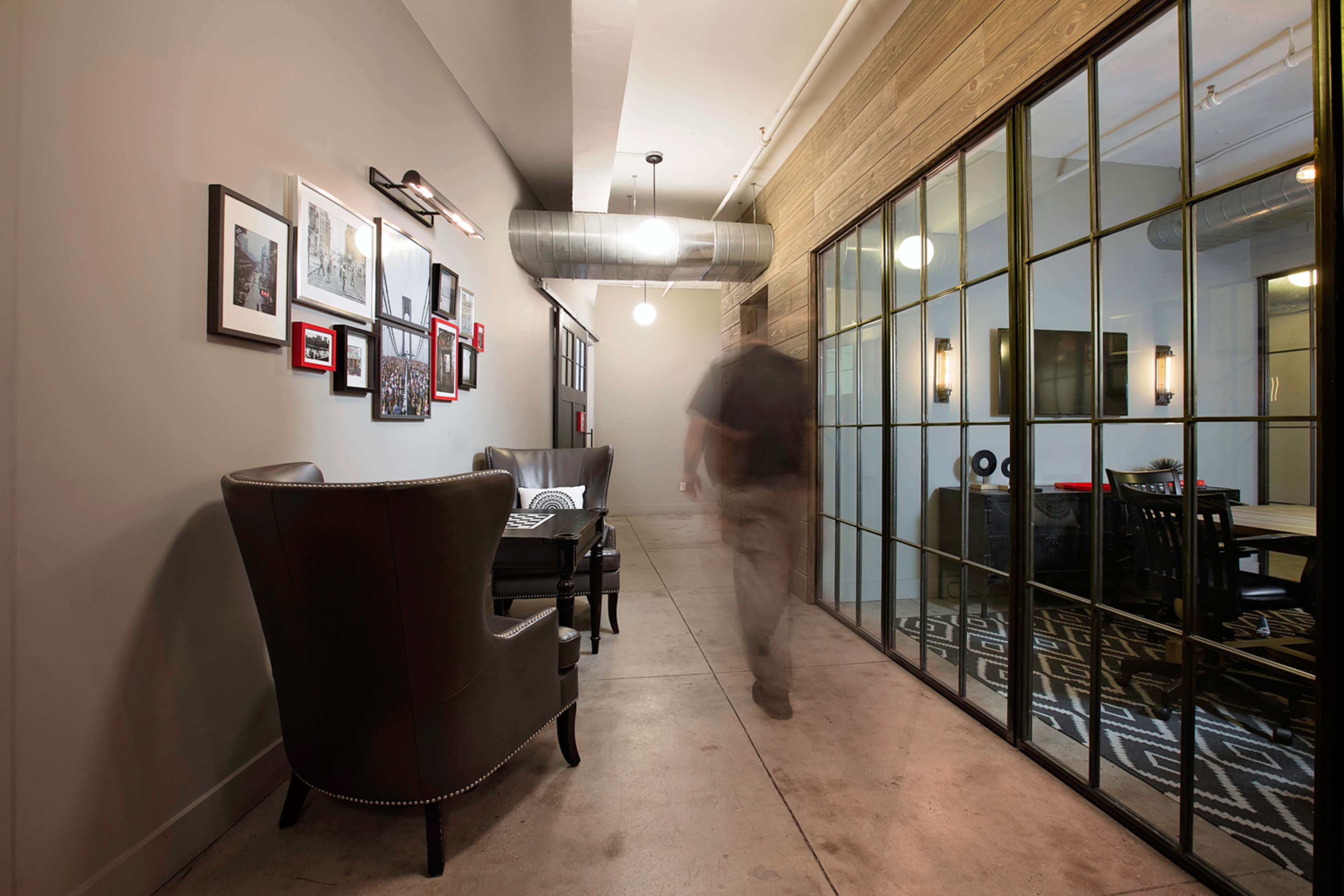 A blurred figure walks down a hallway lined with framed photographs and a glass-walled meeting room.