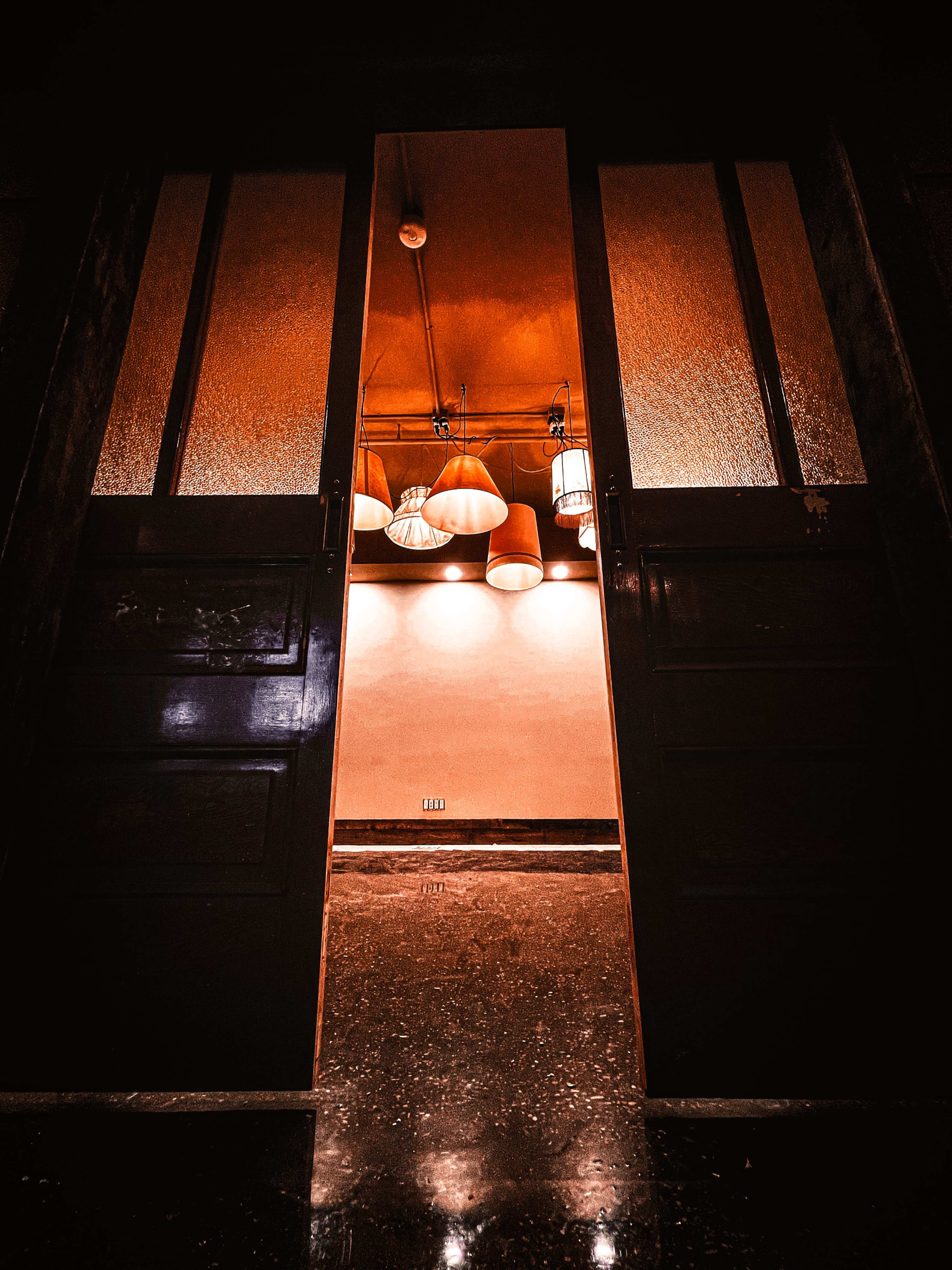 A pair of open doors reveals a well-lit interior with hanging lamps and a smooth floor.