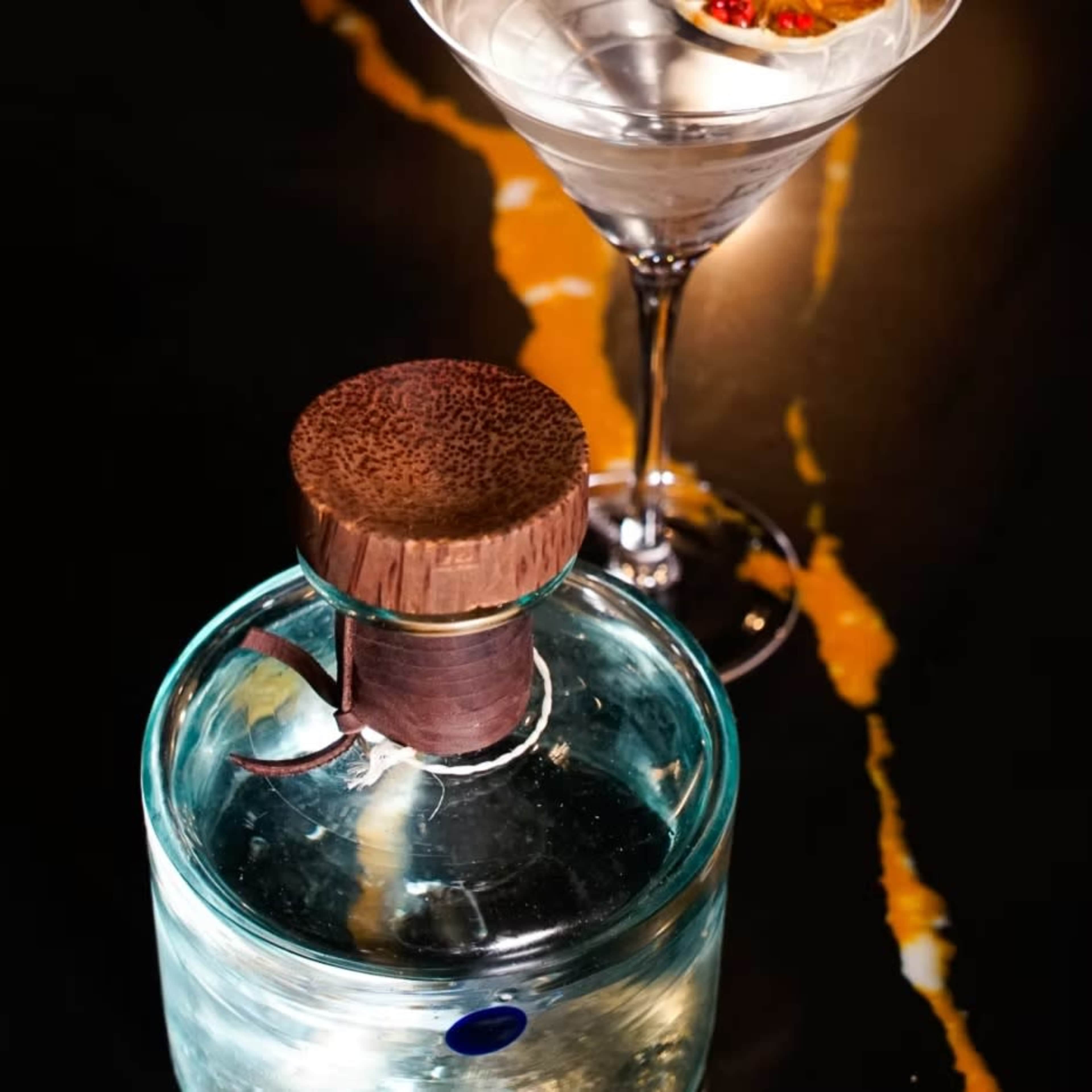 A glass decanter with a wooden stopper sits next to a martini glass on a dark, marbled surface.