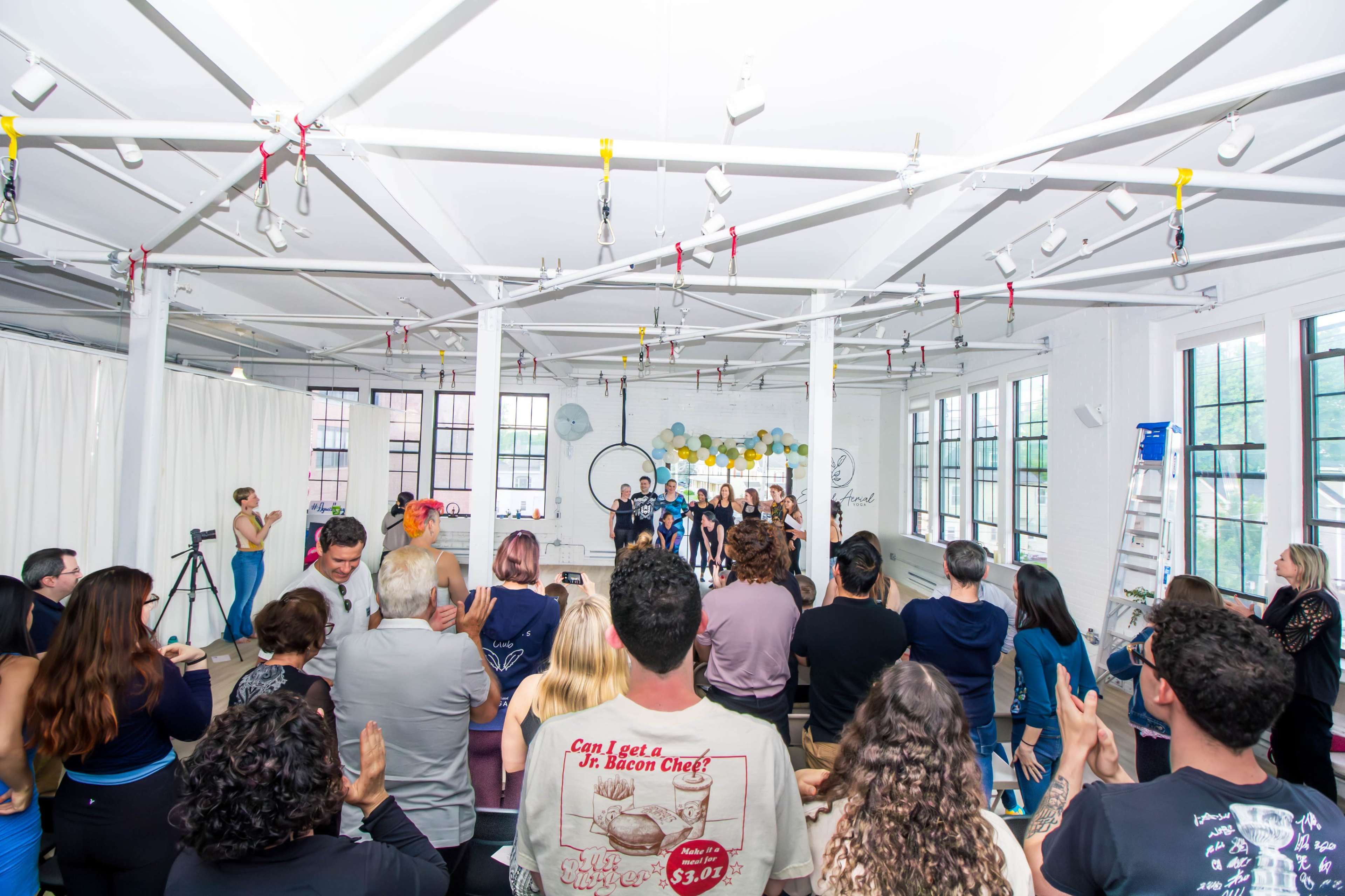 A large group of people is gathered in a bright, spacious room with white walls and large windows for an event or presentation.