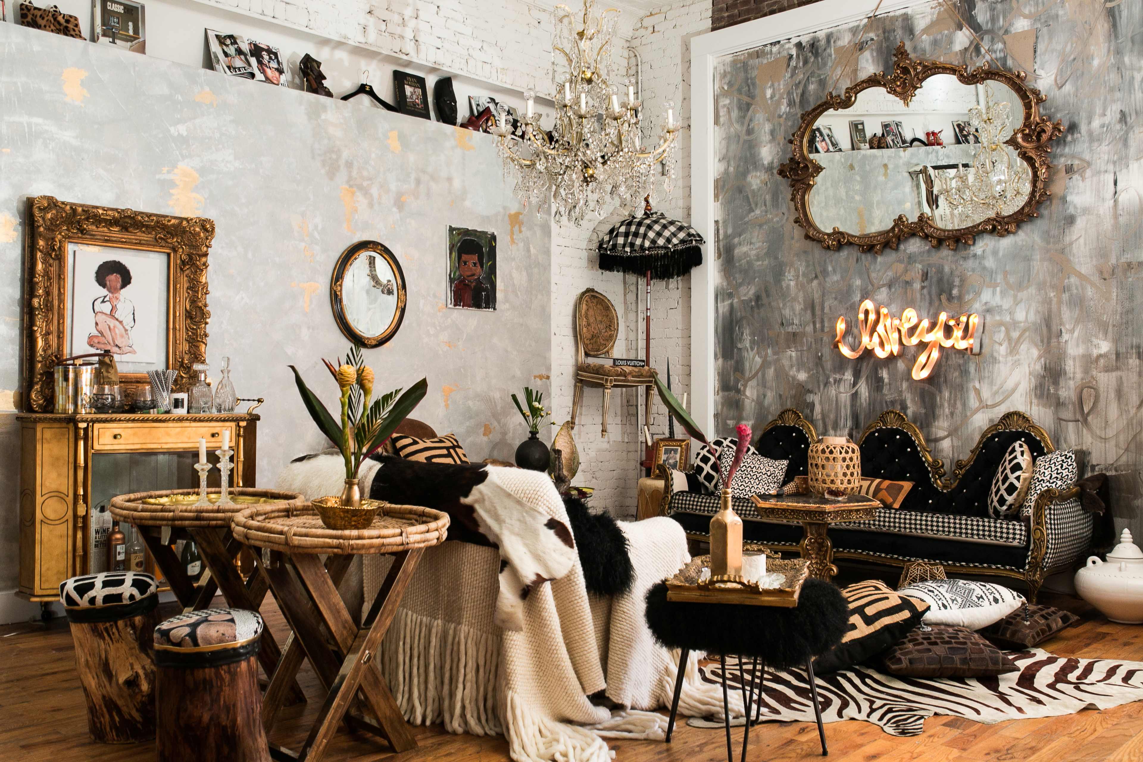 A stylish living room with a mix of vintage and modern decor, featuring a black and gold sofa, a chandelier, and textured wall art.