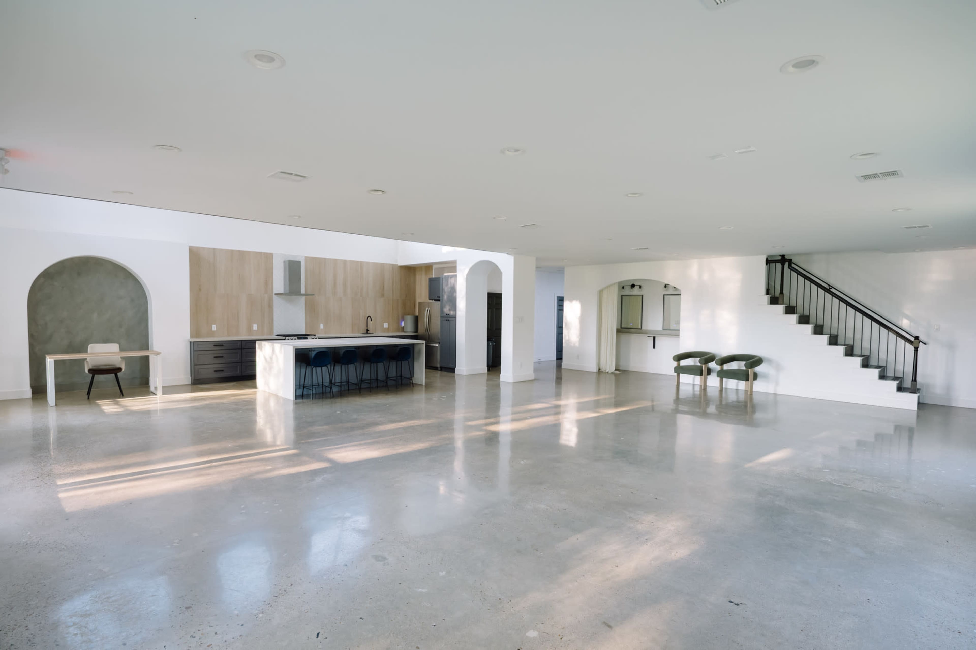 The image shows a spacious, modern living area with a kitchen, dining table, and staircase.