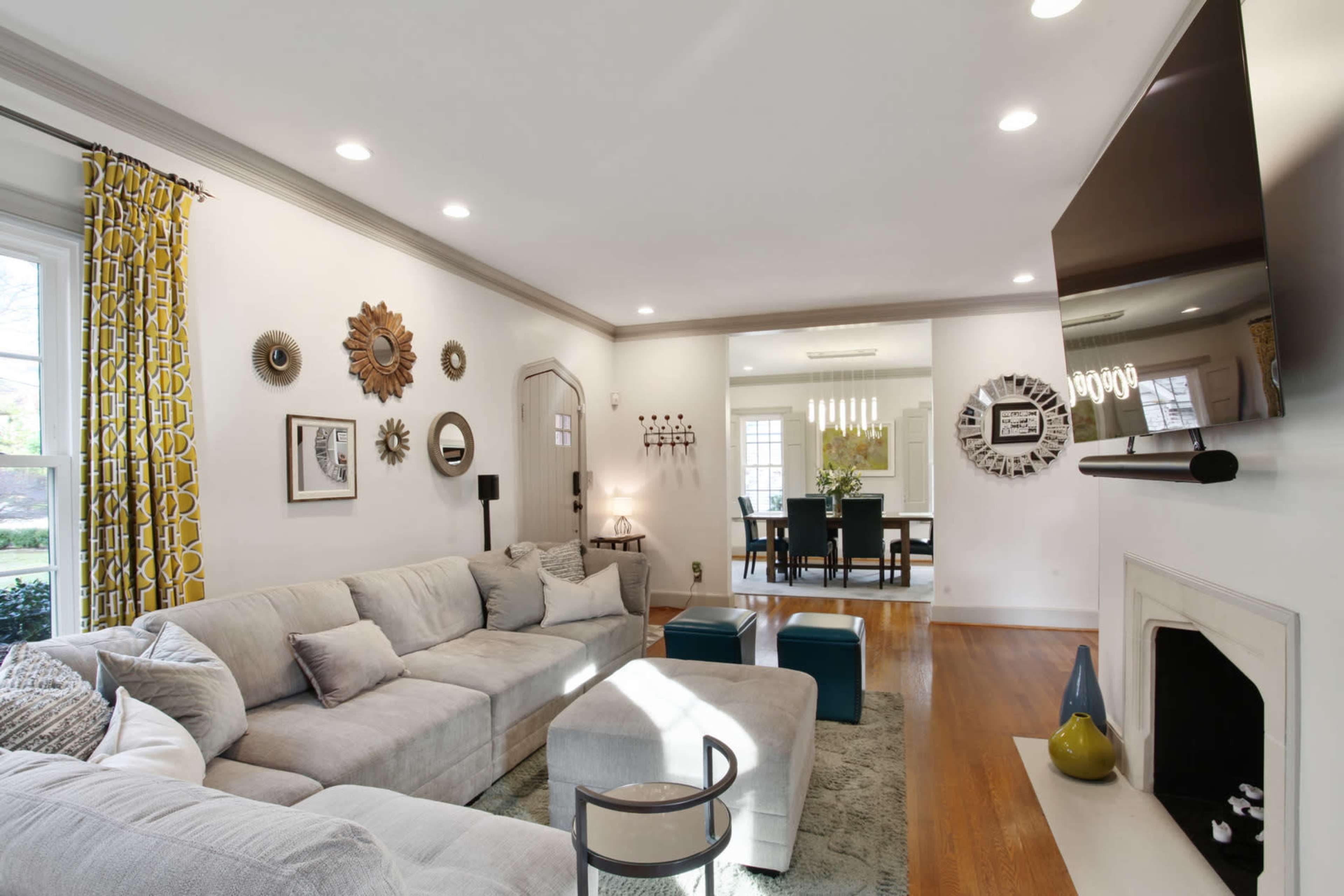 The image shows a modern living room featuring a large sectional sofa, a coffee table, a mounted television, and decorative mirrors on the walls.