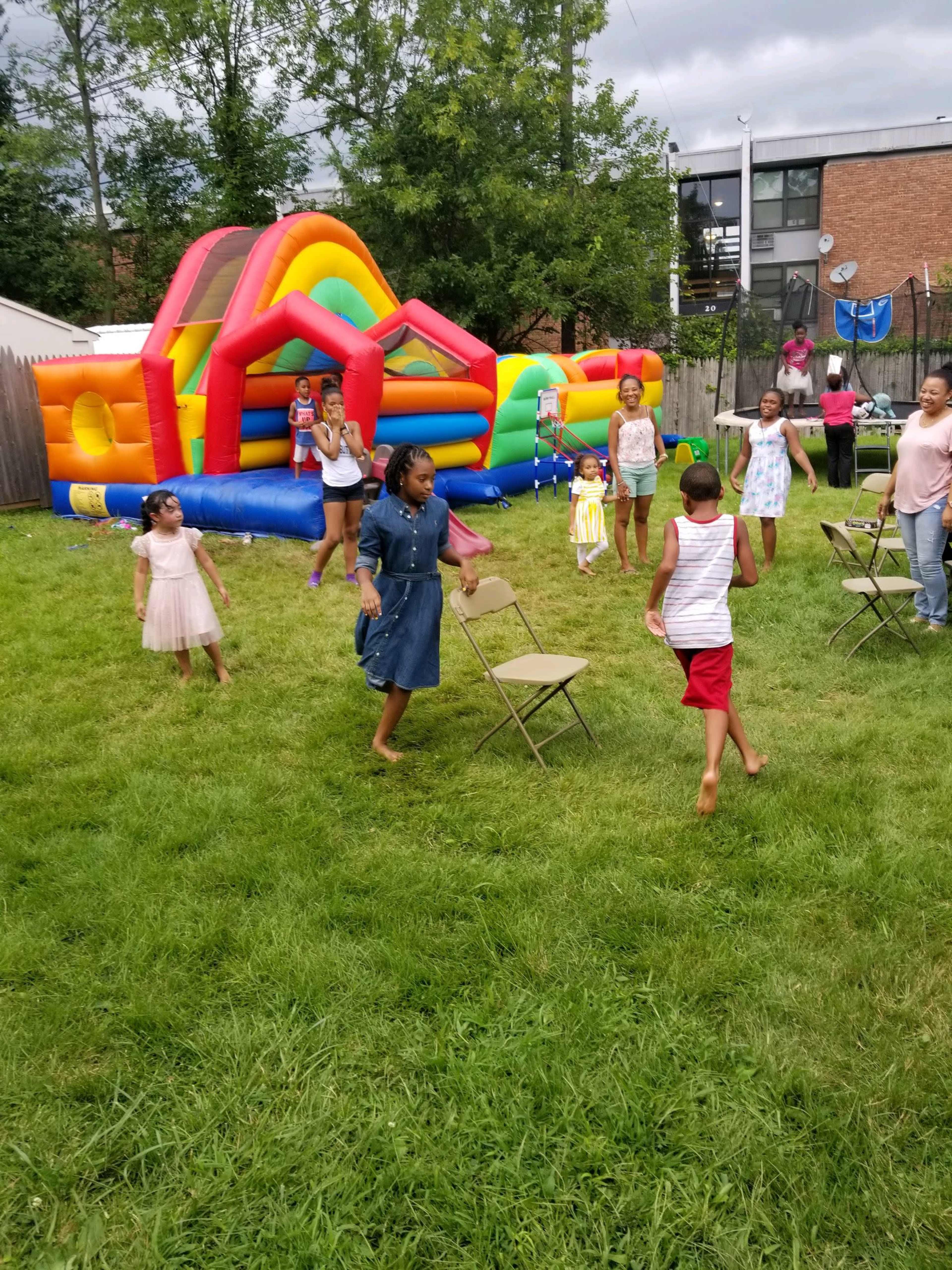 Children are playing in a backyard with a bright inflatable bounce house and several folding chairs set up on the grass.