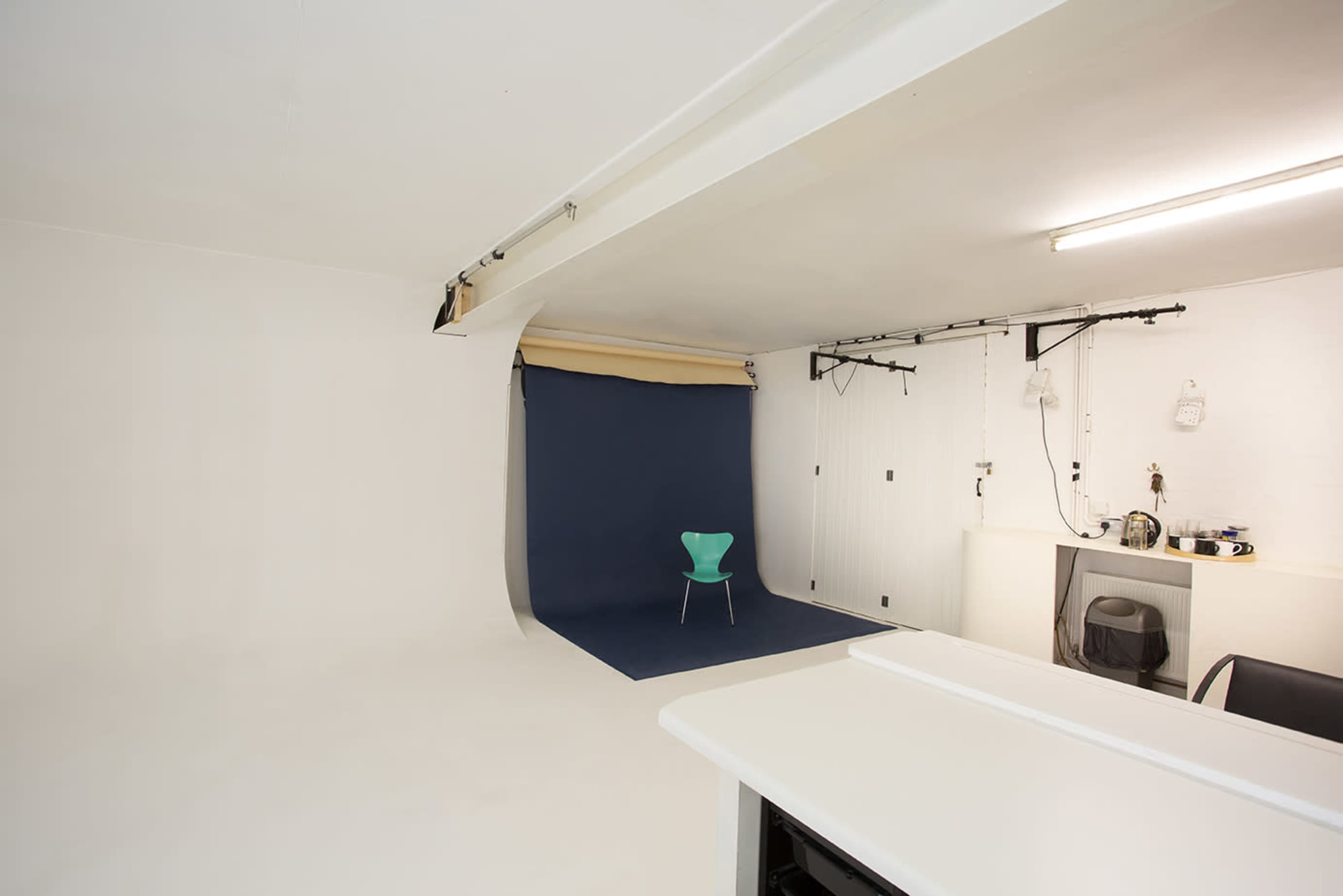 A minimalist photo studio features a blue backdrop, a green chair, and white walls with overhead lighting.