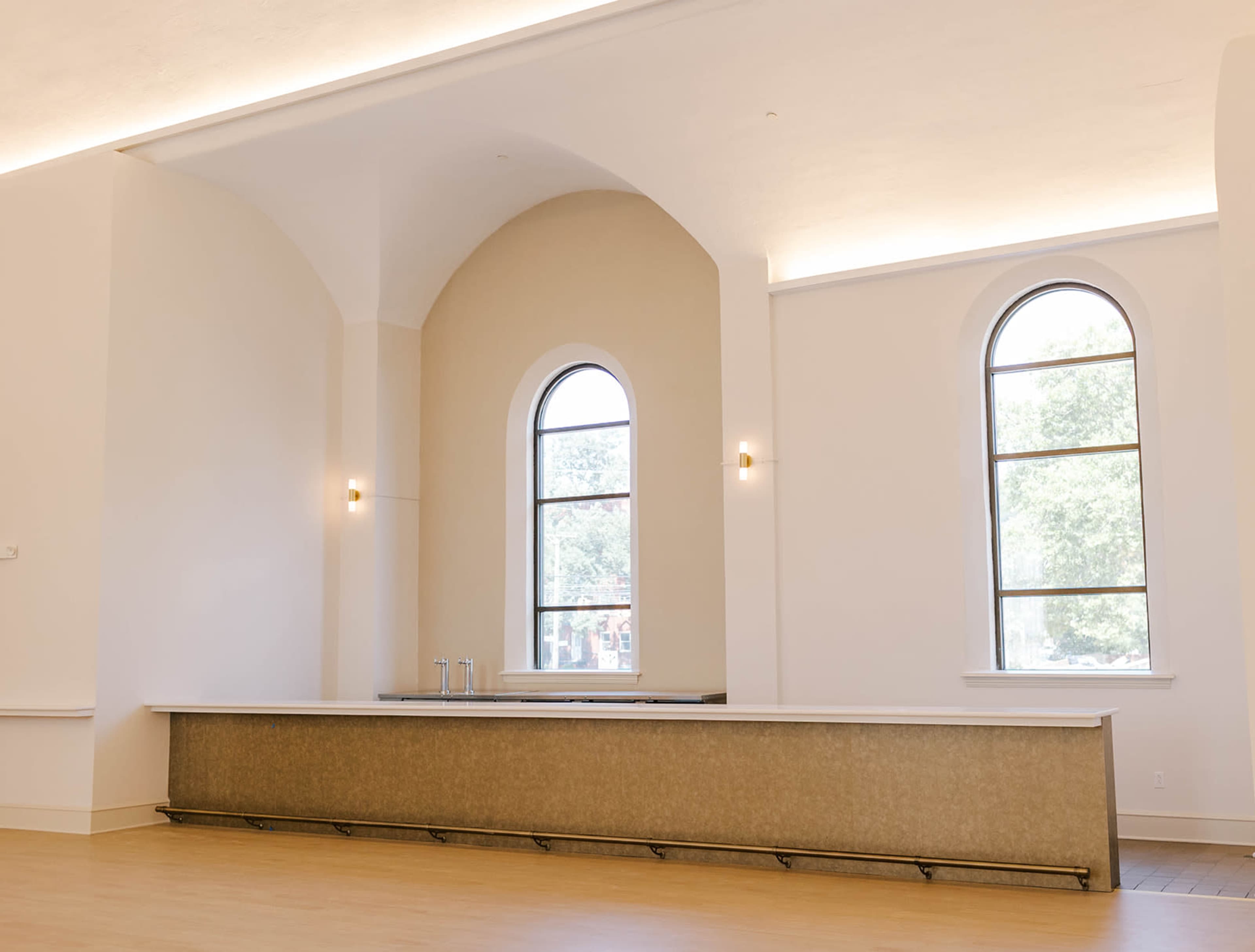 The image shows a spacious room with a long counter and large arched windows allowing natural light to enter.