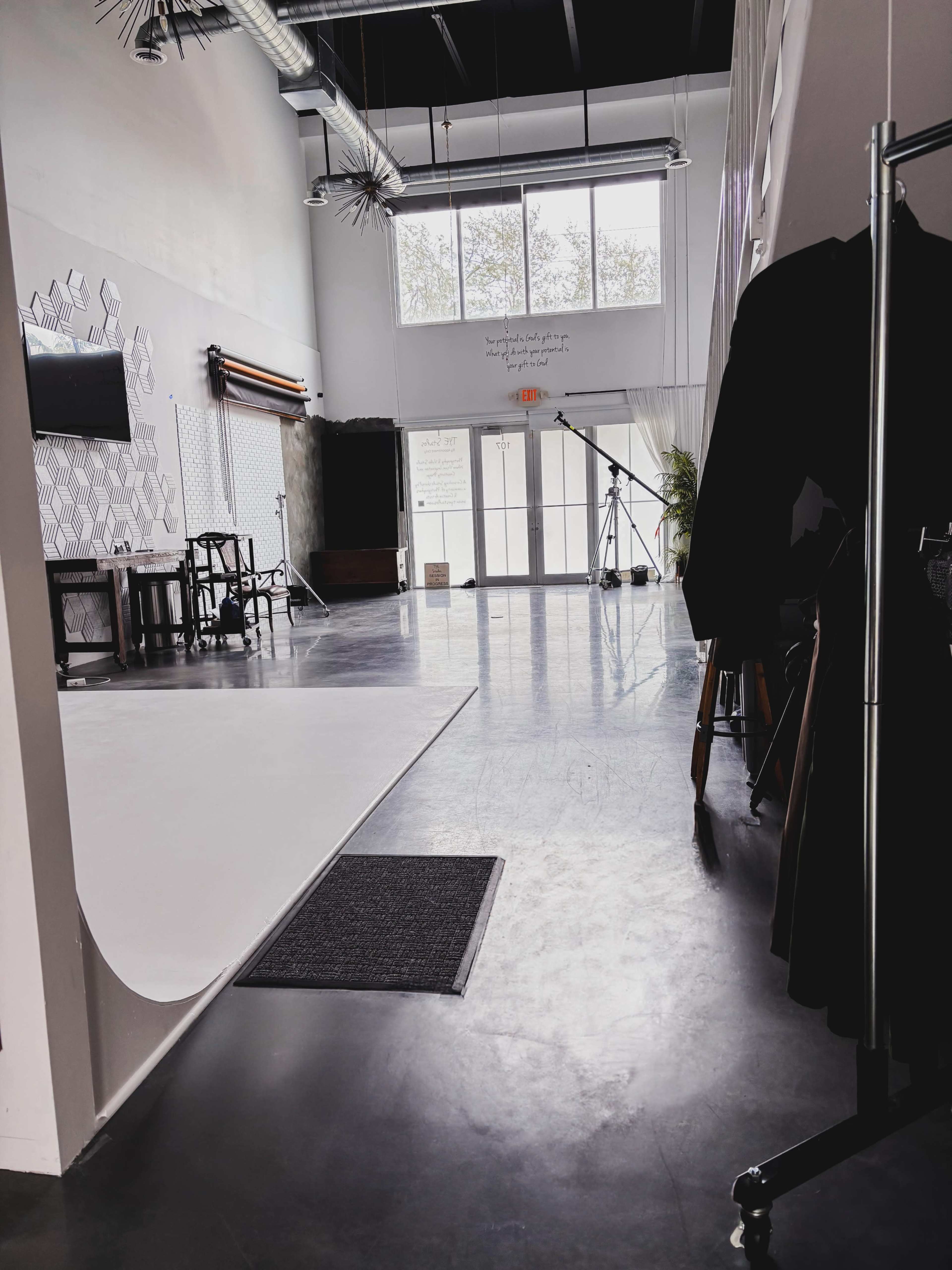 The image shows the interior of a photography studio featuring a large white backdrop, sleek concrete floors, and large windows letting in natural light.