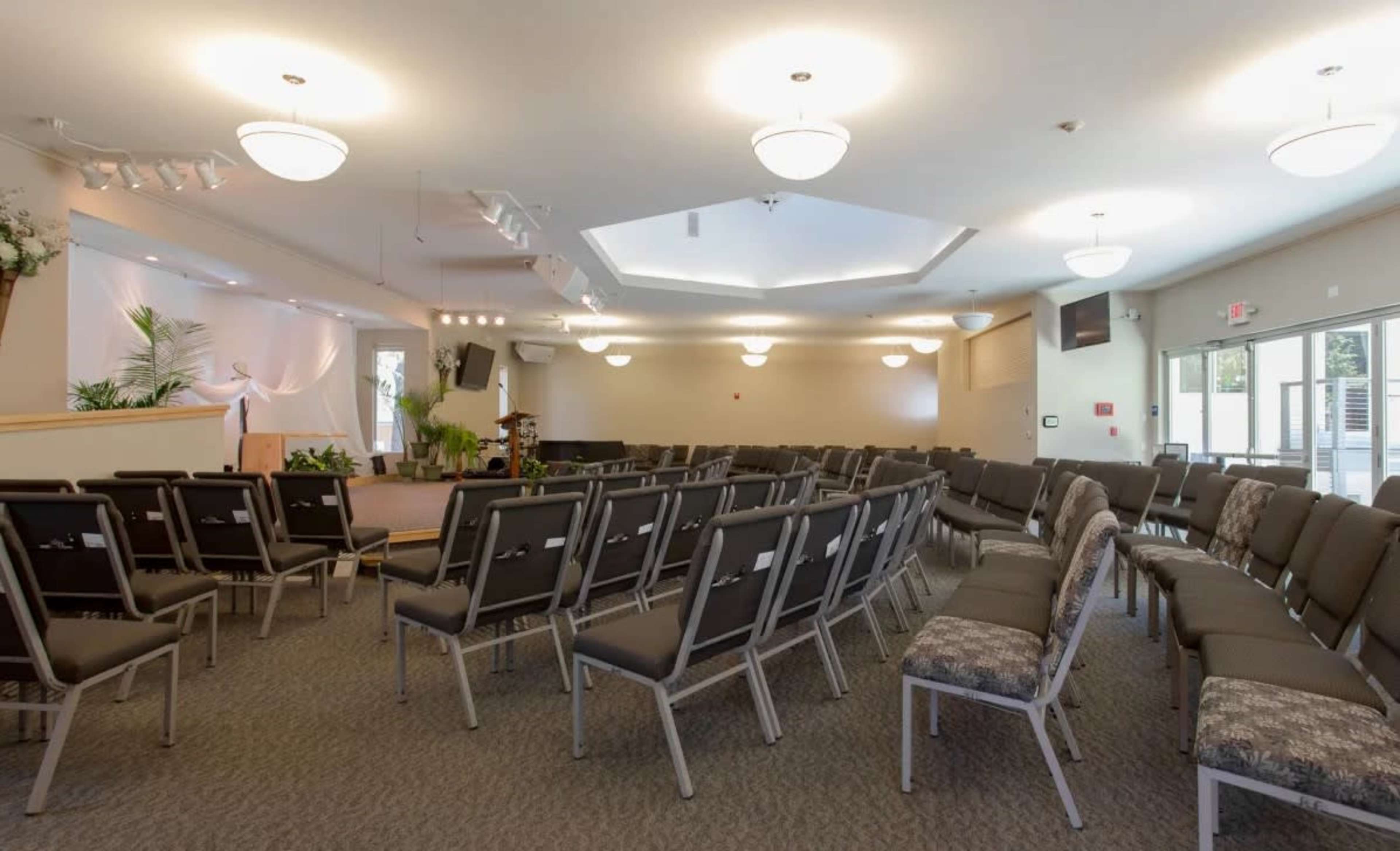 A spacious interior of a hall featuring multiple rows of gray chairs arranged towards a stage at the front.