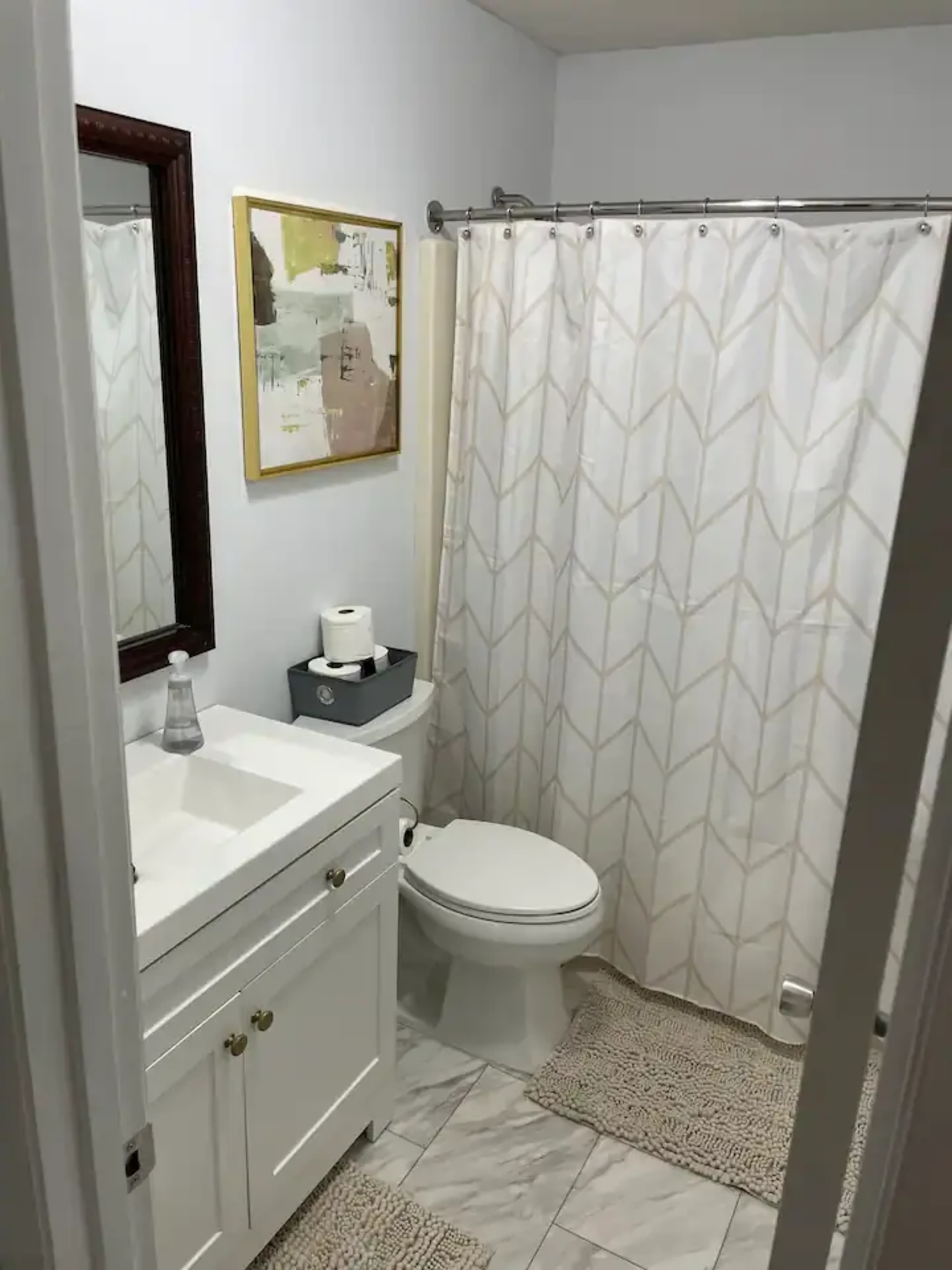 A small bathroom featuring a white vanity, a toilet, a shower curtain with a geometric pattern, and a framed piece of art on the wall.