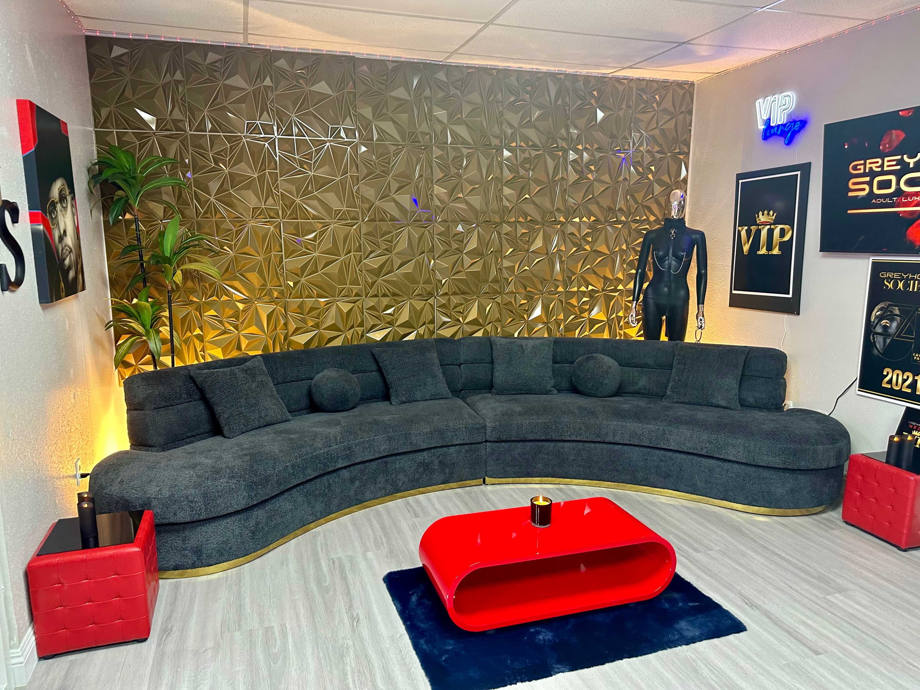 A modern lounge area featuring a curved gray couch with round pillows, a red coffee table, and decorative wall elements.