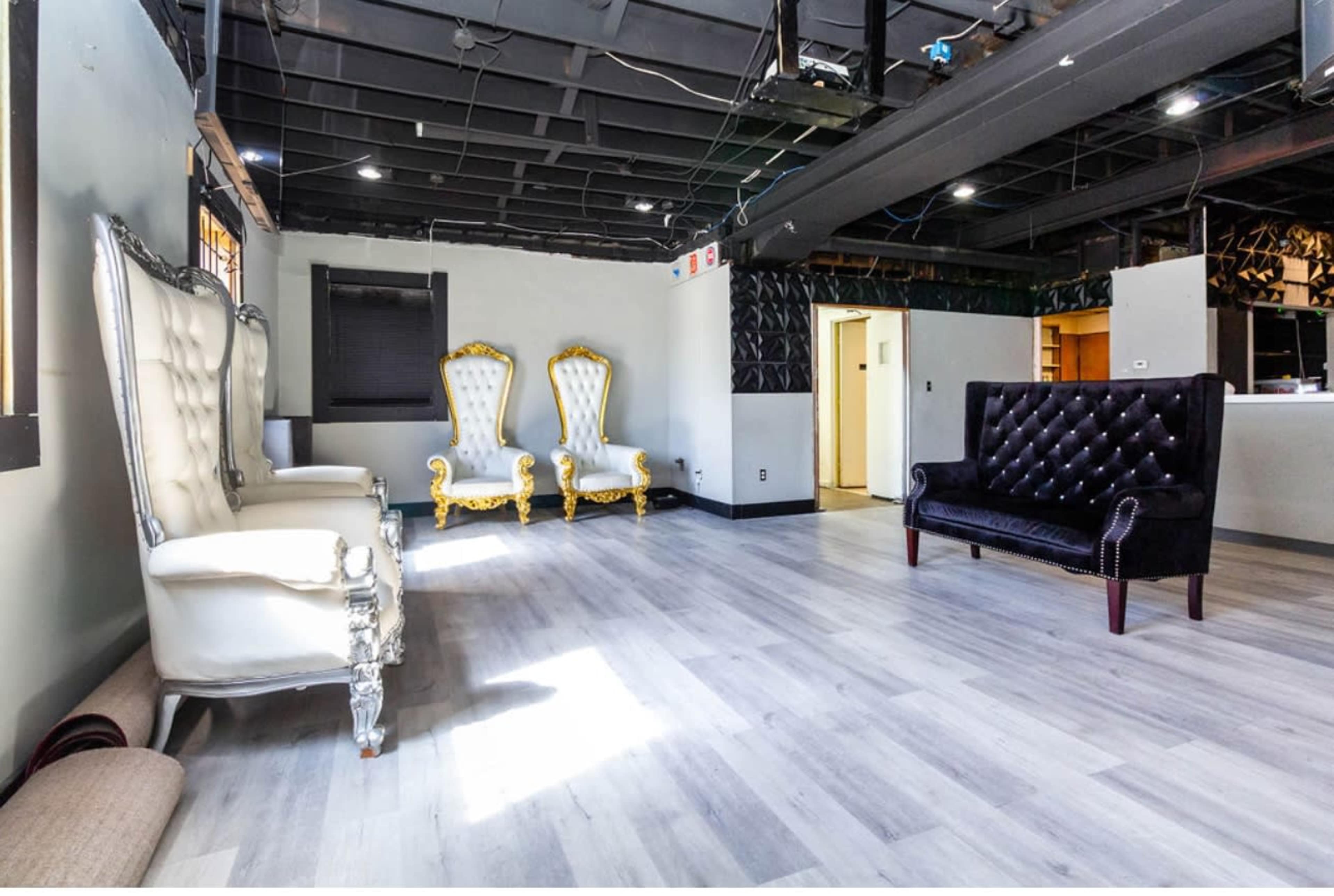 The image shows a spacious, minimally furnished room with two ornate white chairs and one black tufted sofa.