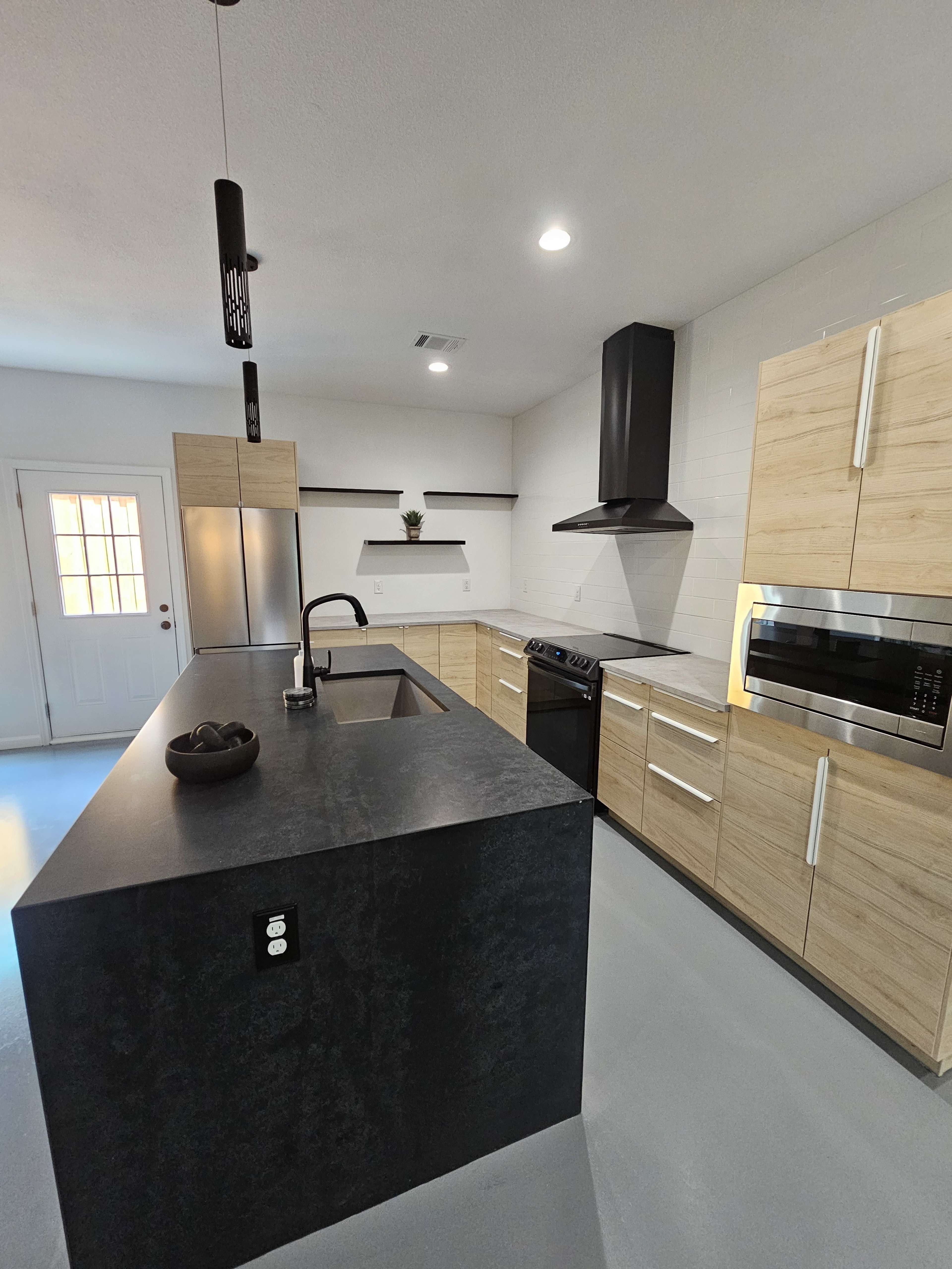 A modern kitchen with a central island, stainless steel appliances, and wooden cabinetry, illuminated by overhead lighting.