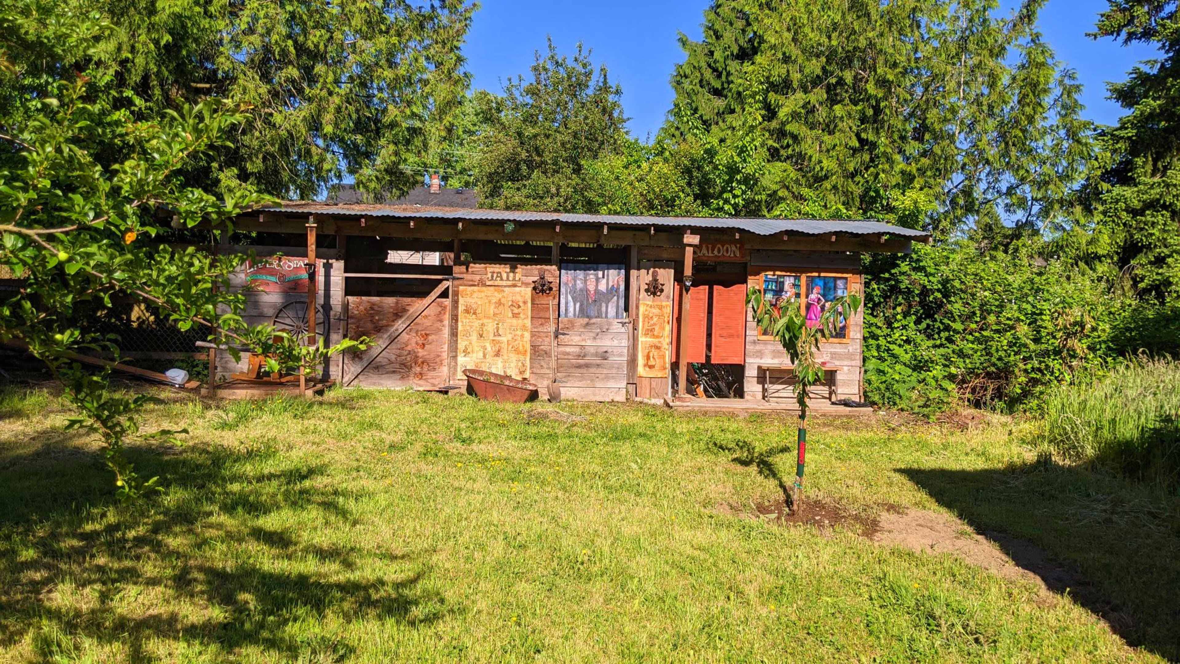 A rustic wooden building with various decorations and signs, set against a backdrop of greenery and a clear blue sky.