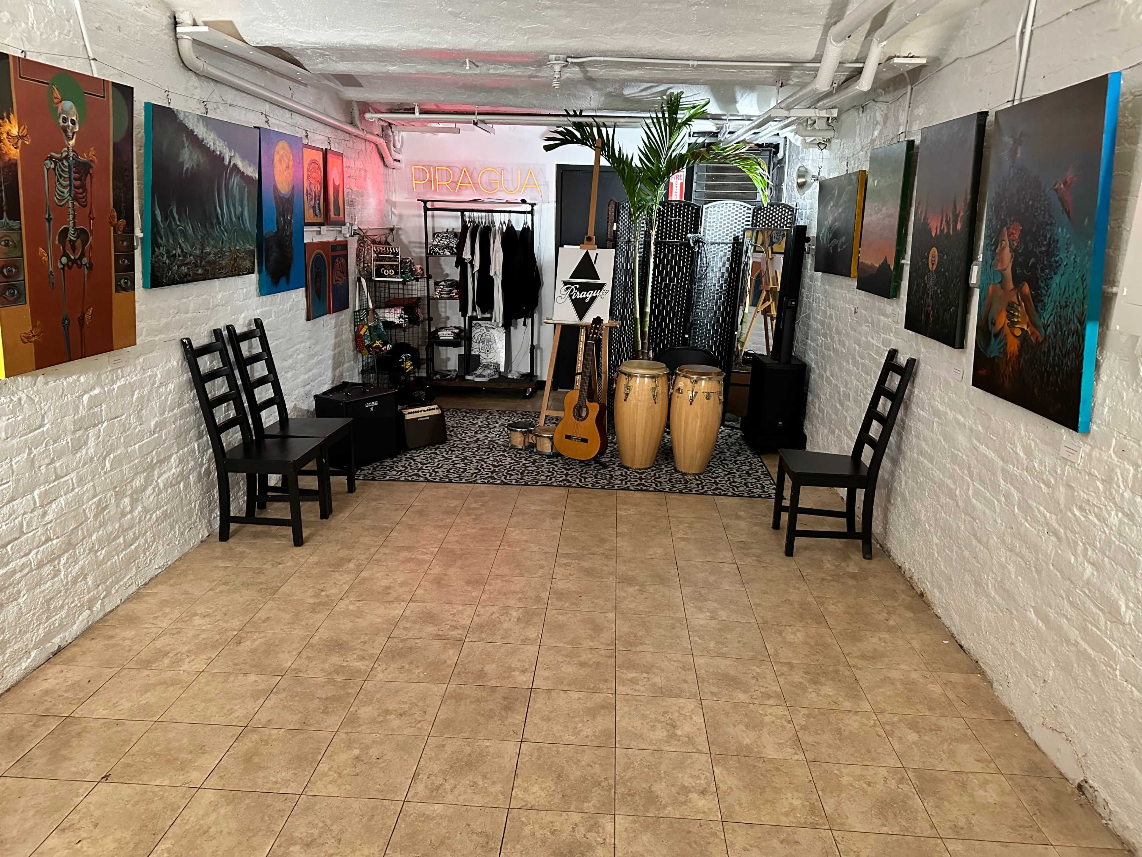 An art space with two empty chairs facing a collection of colorful paintings on the walls, musical instruments, and decorative elements.