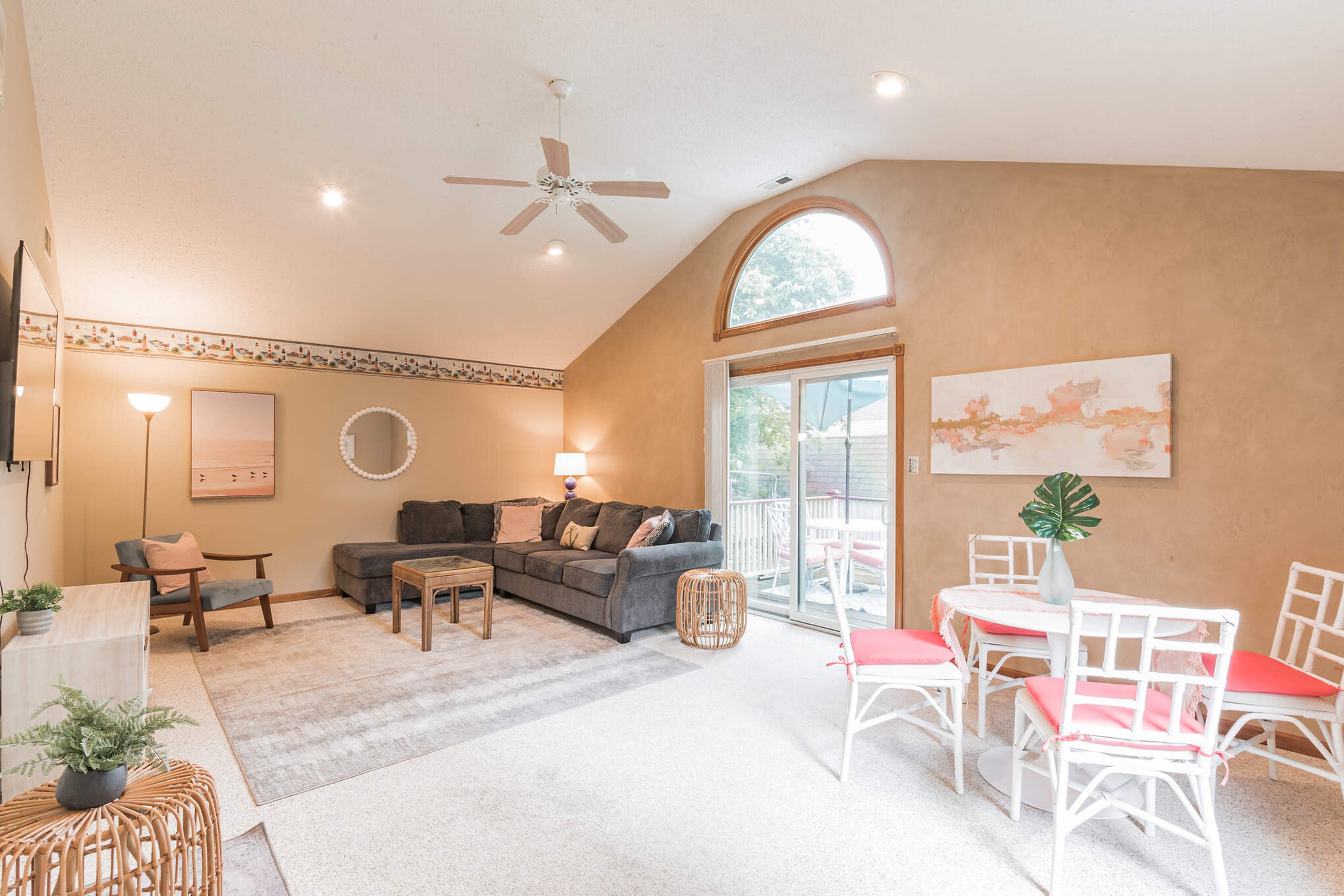 A cozy living room features a sectional sofa, a wooden coffee table, and a dining area with a round table and chairs, illuminated by natural light from a large window.