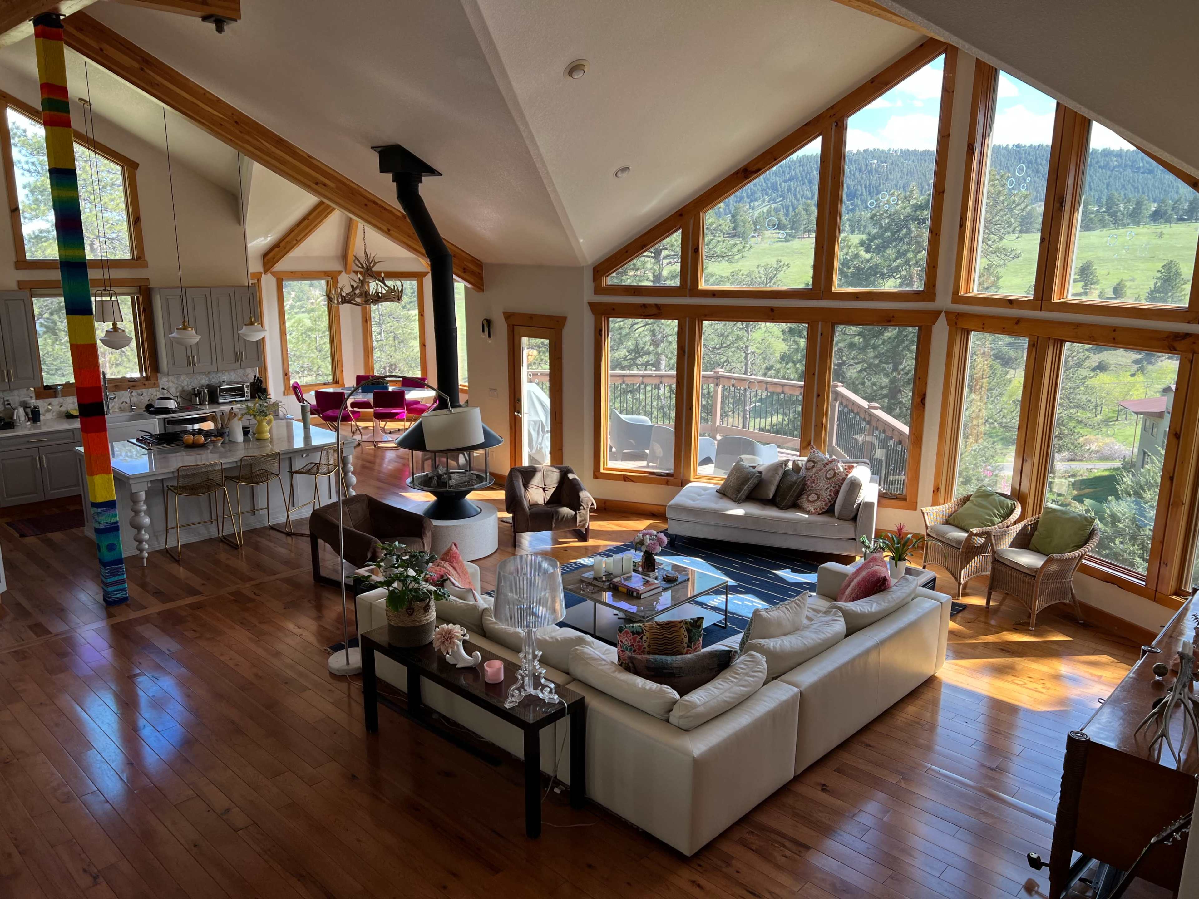 The image depicts a spacious, open-concept living area with large windows offering a view of green hills and trees.